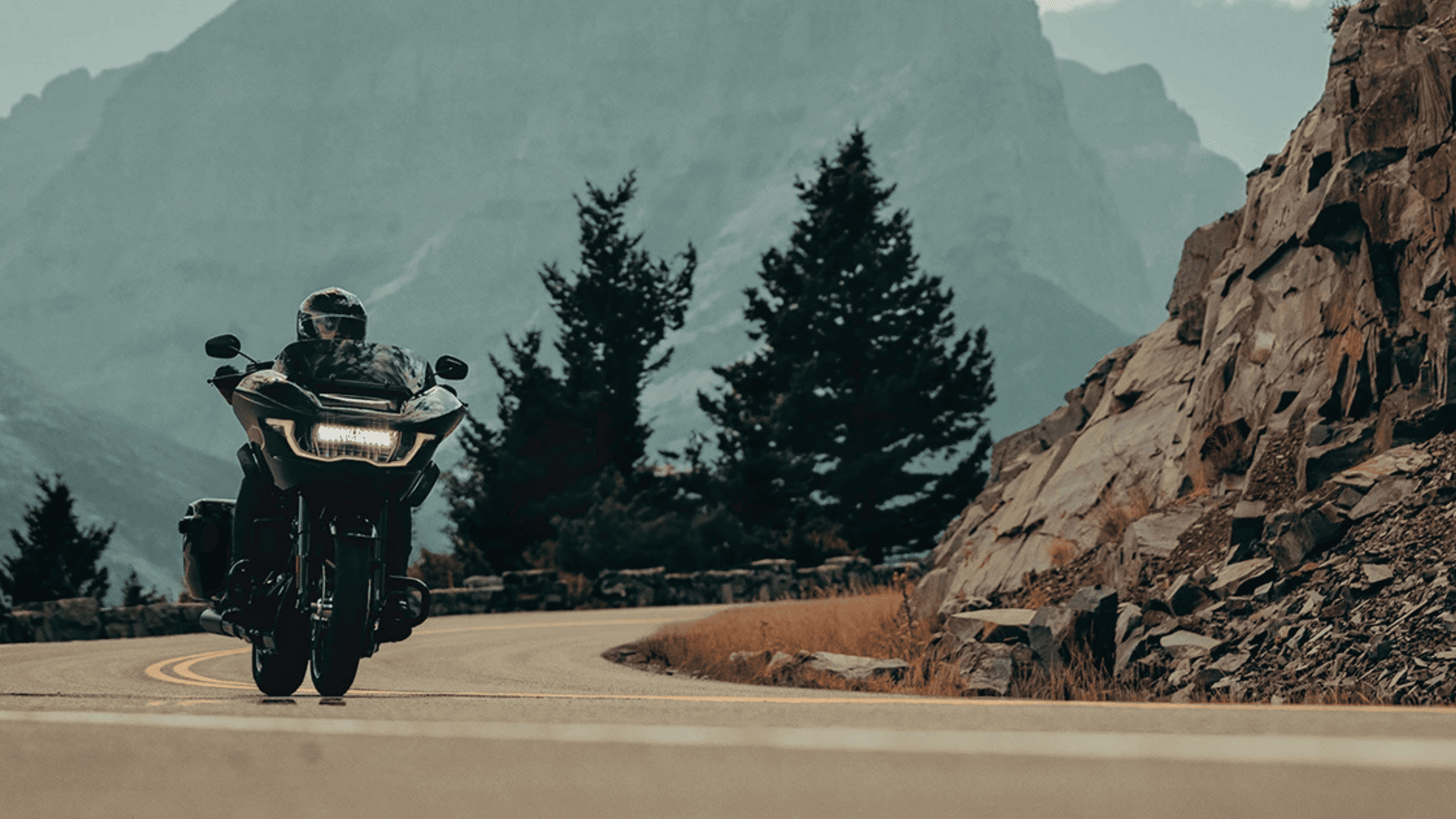 2025 Harley-Davidson Road Glide® riding through mountain curve with LED headlamp glowing