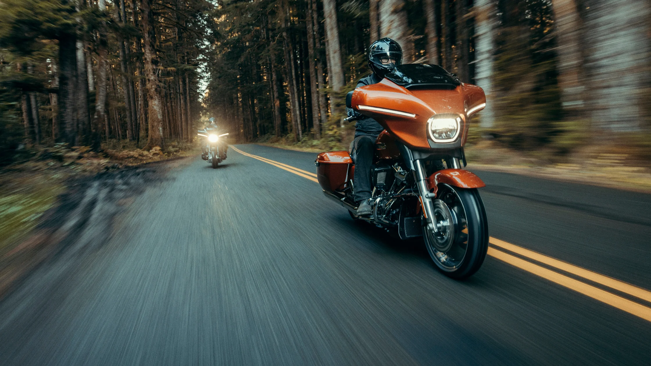 2025 H-D® Street Glide® Carryover in orange riding through dense forest, front side view, rider in black gear