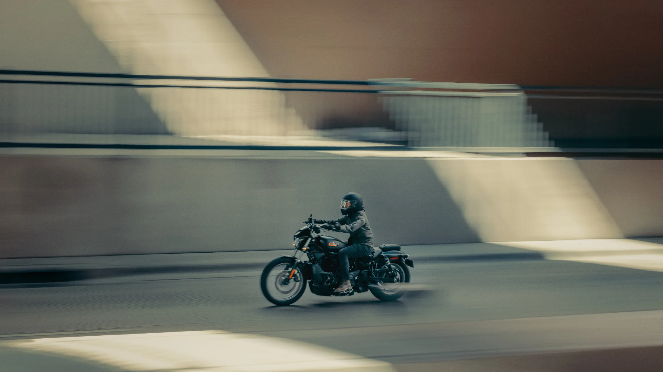 2025 Nightster S in black with rider in helmet riding through urban street in motion blur.