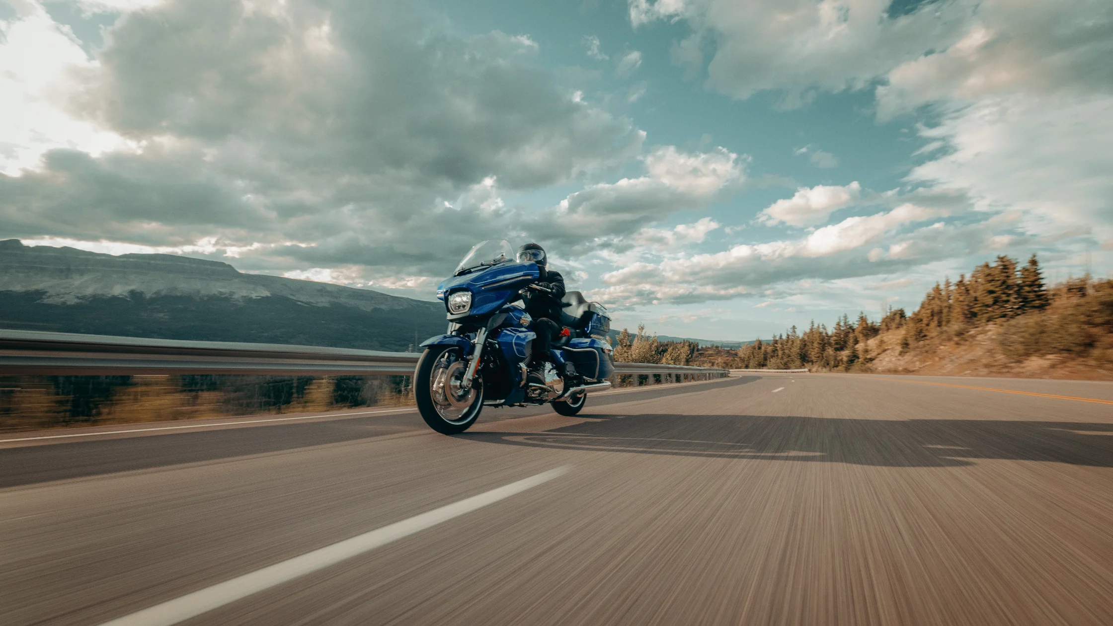 2025 Street Glide Ultra in blue cruising open highway with scenic mountain background, dynamic angle.