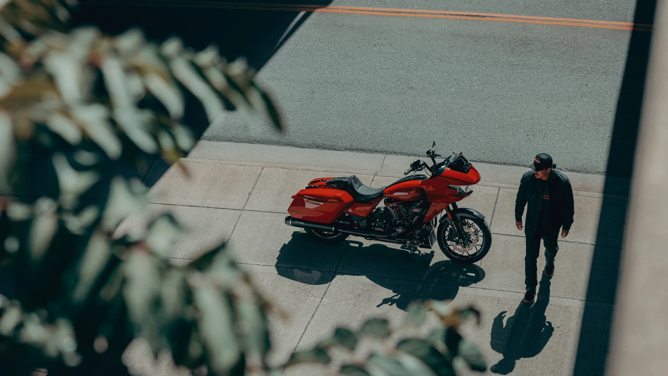 Top-down view of 2025 CVO Road Glide ST in red, parked curbside in urban setting with rider nearby.