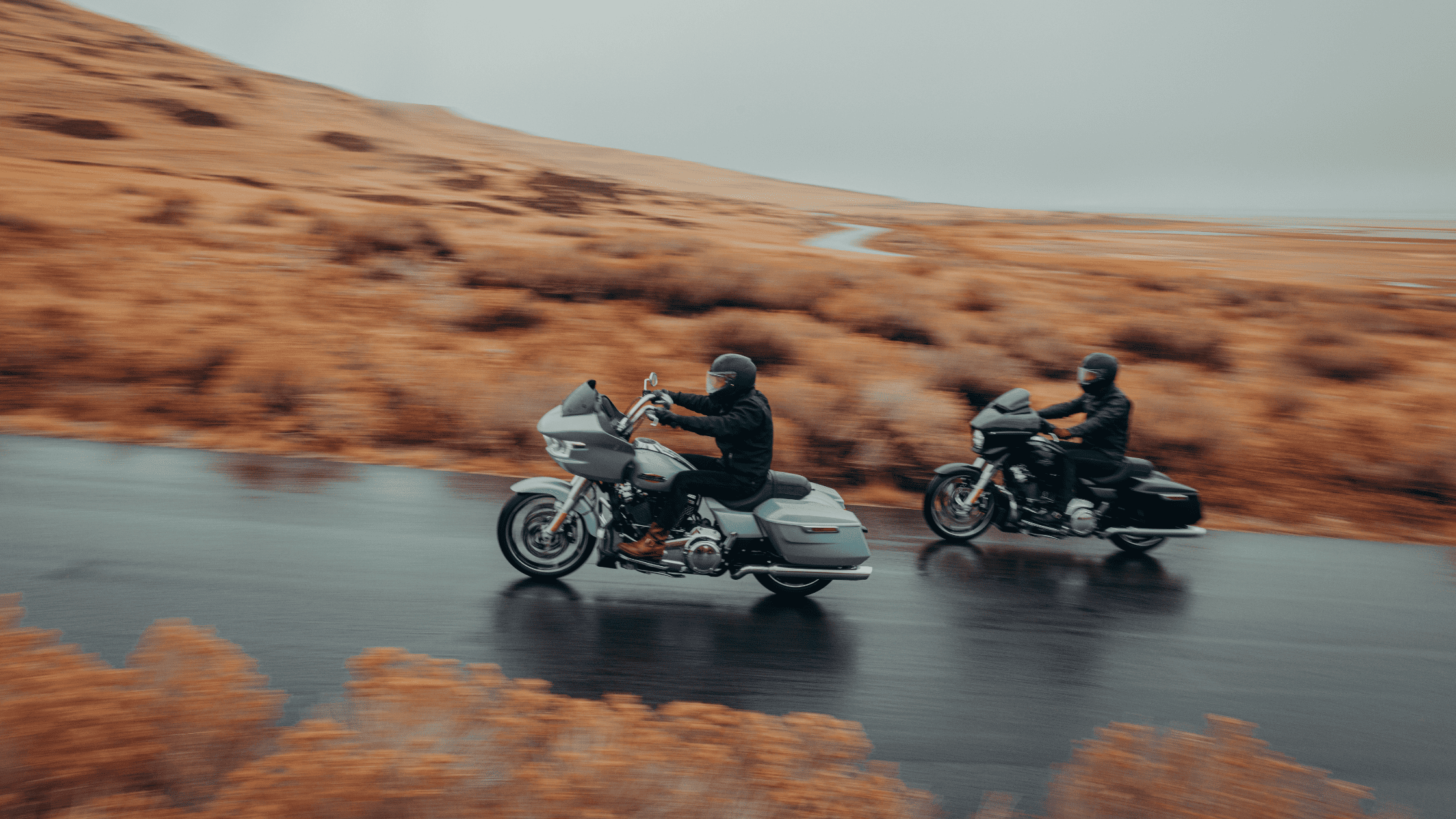 Two riders cruising 2025 Harley-Davidson Road Glide models on wet highway through hills.