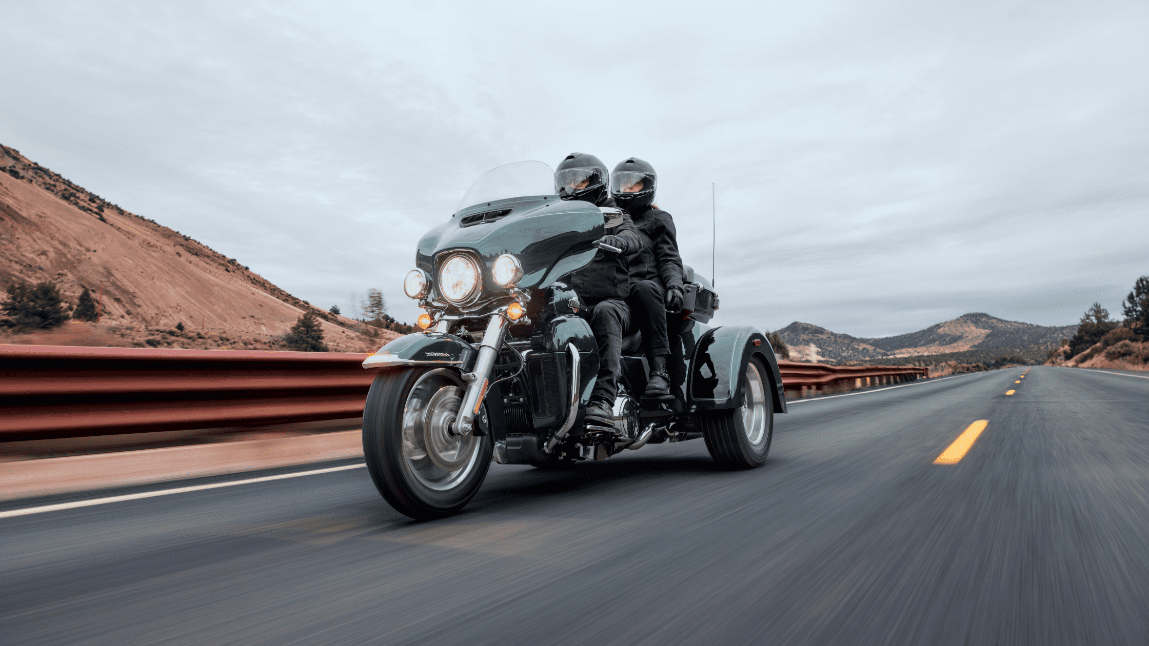 Two-up riders enjoy the open road on a 2025 Harley-Davidson® Tri Glide® Ultra with a spacious King Tour-Pak®, ideal for long-distance touring.