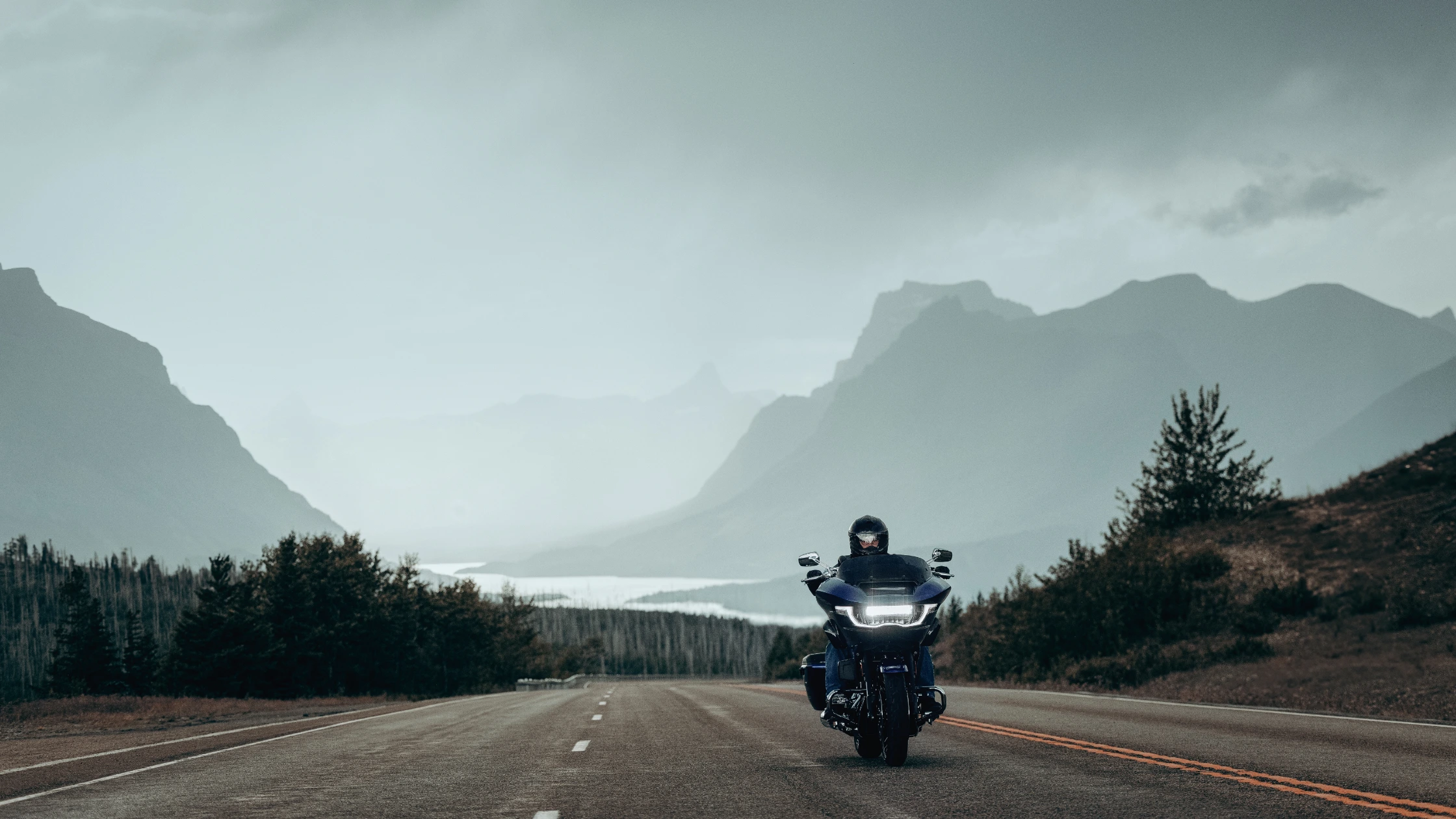 2025 CVO Road Glide in blue ridden on open highway with scenic mountain backdrop.