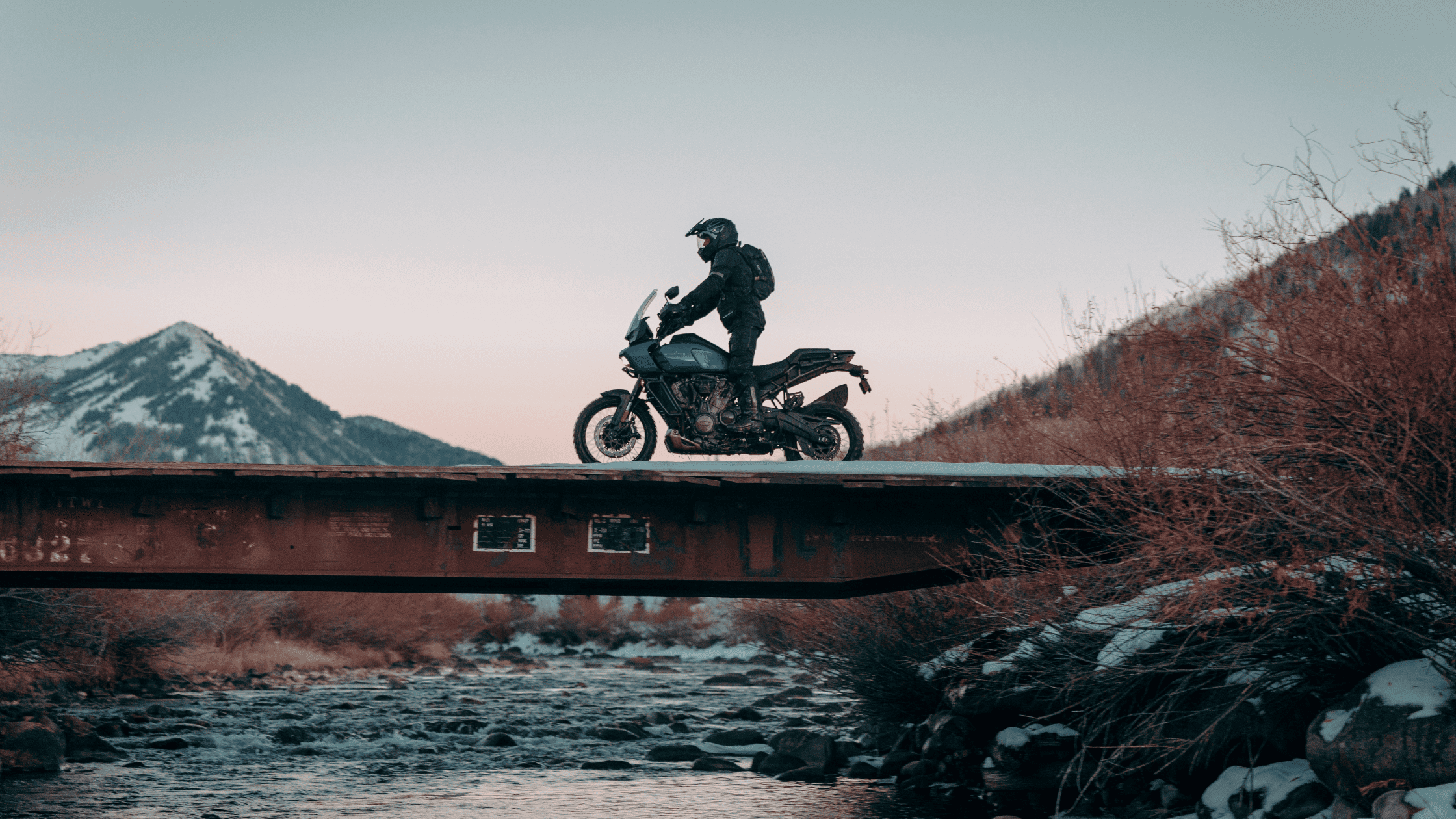 2025 Pan America 1250 Special with rider crossing bridge over river with snow-capped mountains