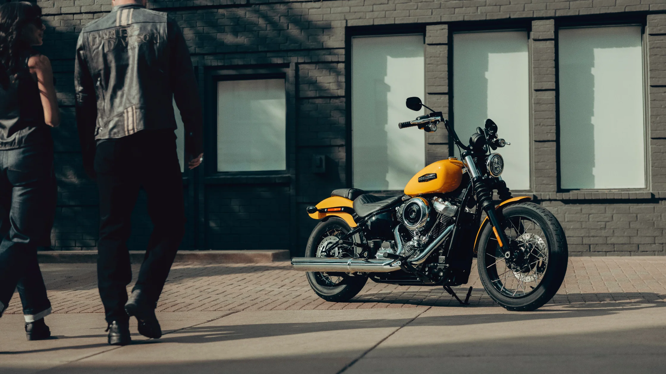 2025 Street Bob motorcycle in bright yellow parked on city street with two people walking past.