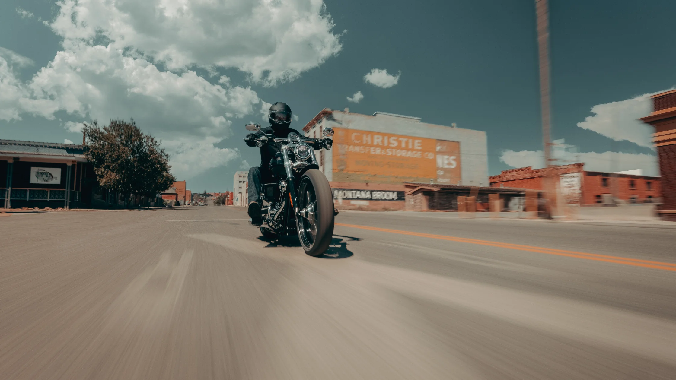Rider on 2025 H-D® Breakout® cruising through downtown with bright sky and motion blur effect
