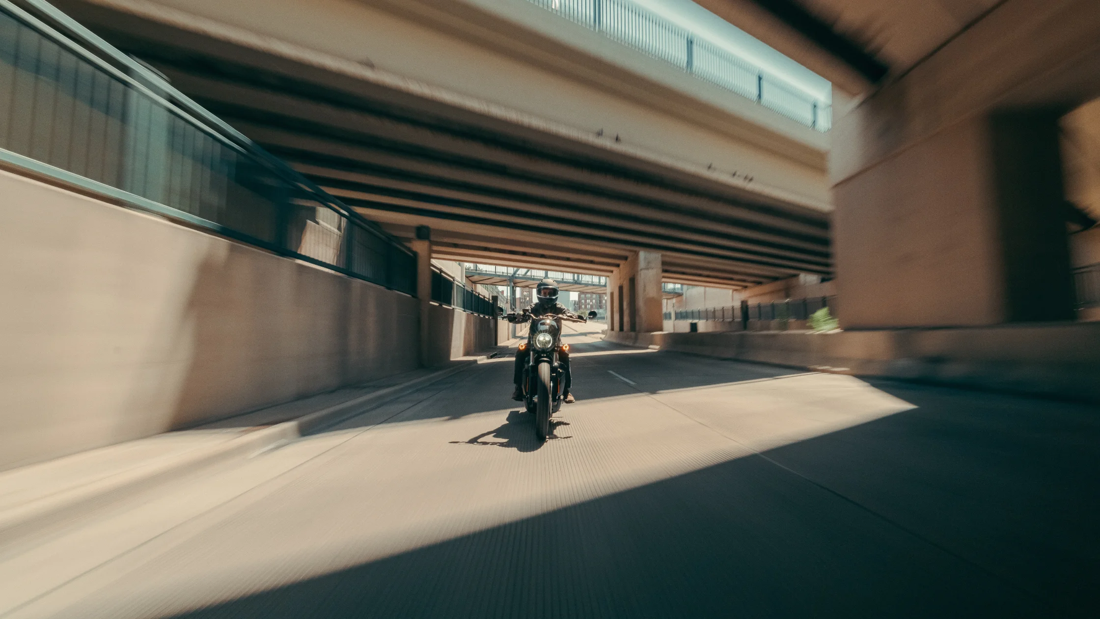 Rider on 2025 H-D® Nightster® S speeding beneath overpass with sharp light and shadow contrast