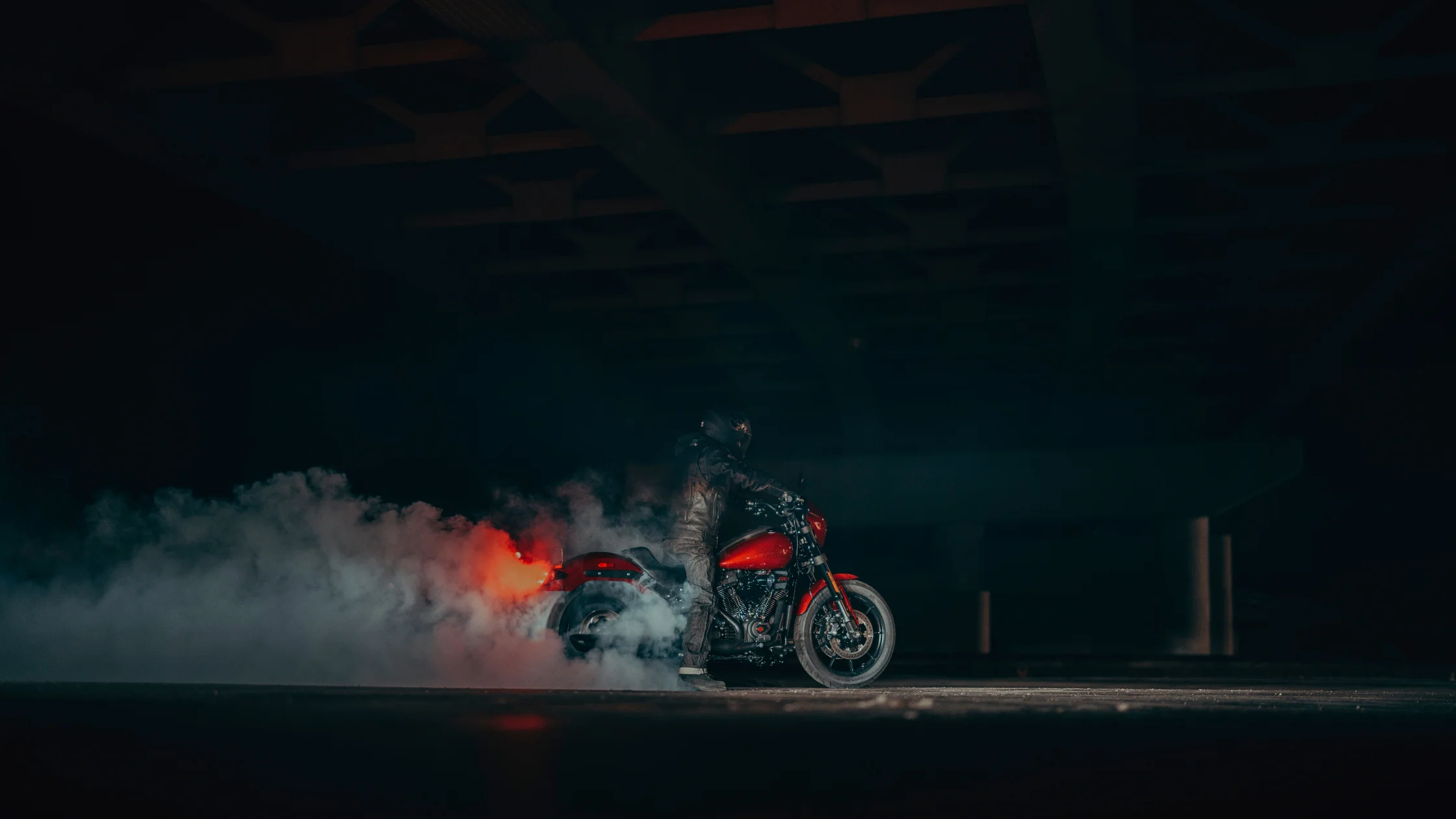 Rider performing burnout on 2025 H-D® Low Rider® S in red with smoke in dimly lit warehouse