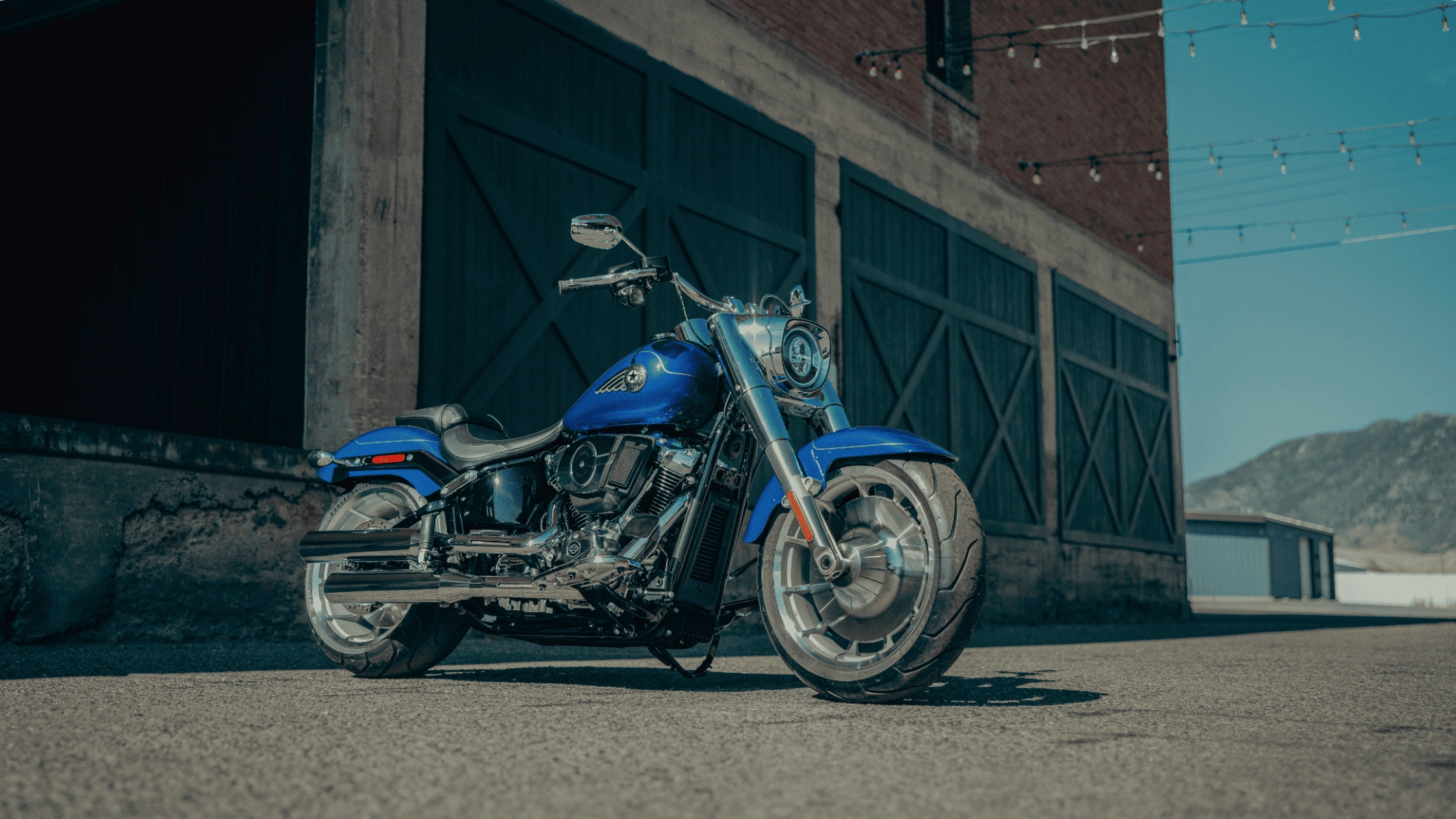 2025 Harley-Davidson Fat Boy near McDonough, GA parked by rustic buildings, featuring classic cruiser styling and solid disc wheels.