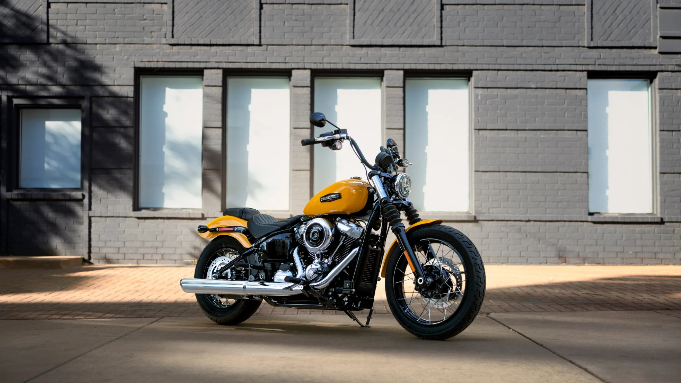 2025 Harley-Davidson® Street Bob® in bright yellow paint parked beside a brick building under sunlight.