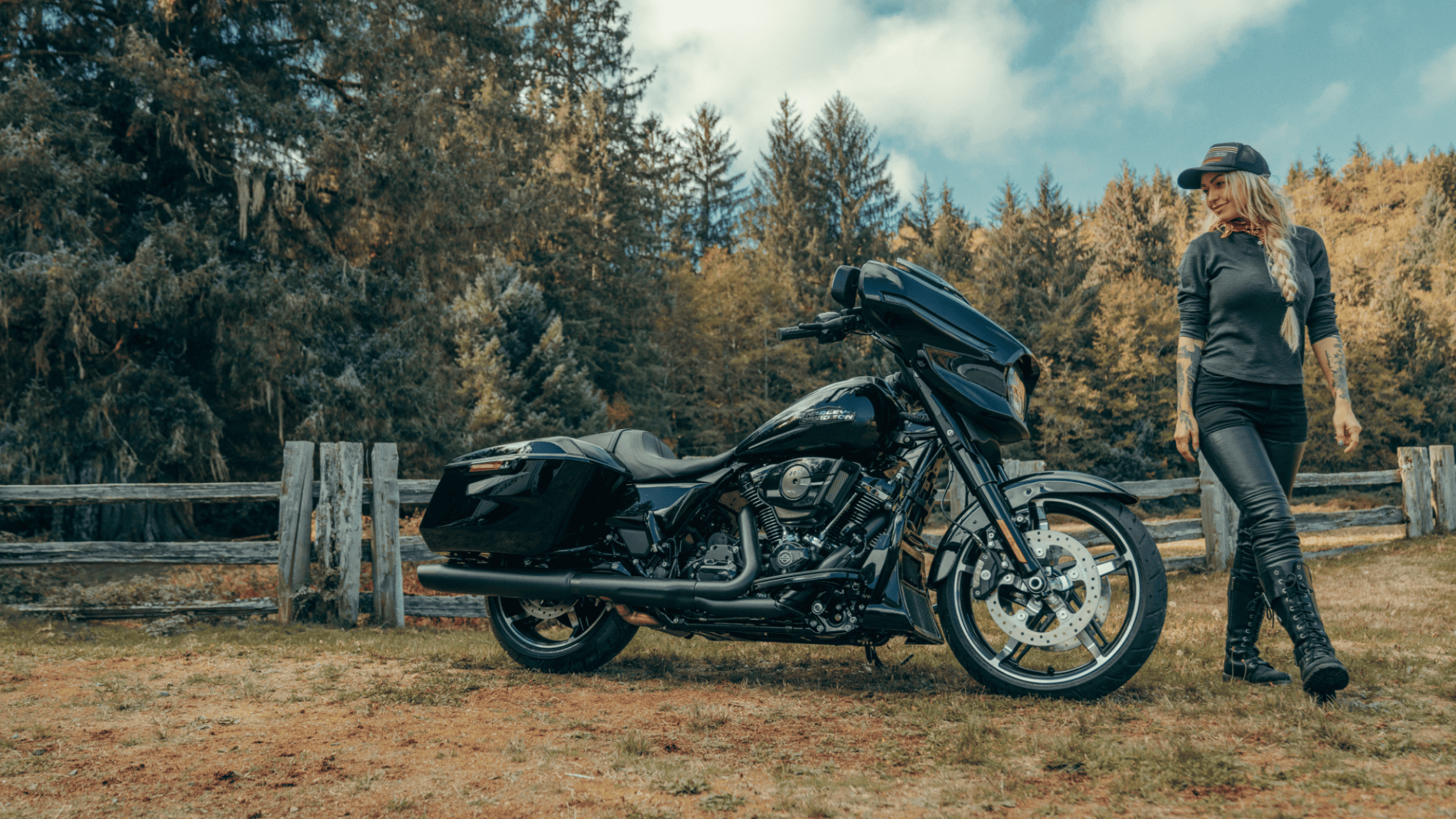 A 2025 Harley-Davidson® Street Glide® bagger is parked beside a wooded fence, showcasing its sleek black fairing, low-slung profile, and premium touring components.