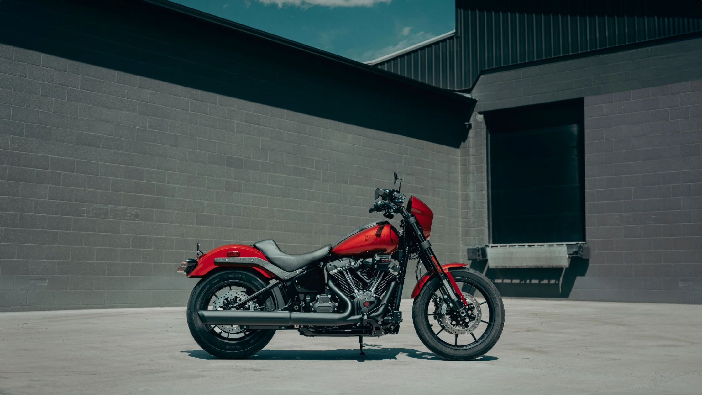 2025 Harley-Davidson Low Rider S in vivid red parked near industrial wall under clear sky.