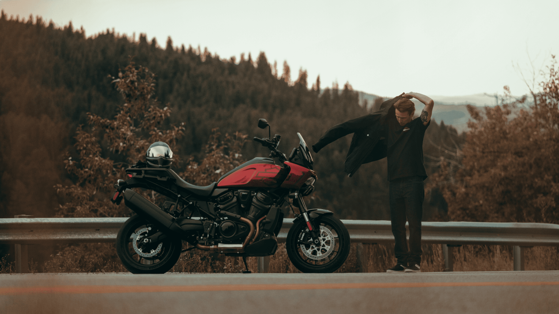 A red 2025 Harley-Davidson® Pan America® 1250 ST positioned along a mountain highway with a rider preparing for a ride, highlighting its power, endurance, and adventure-ready performance.