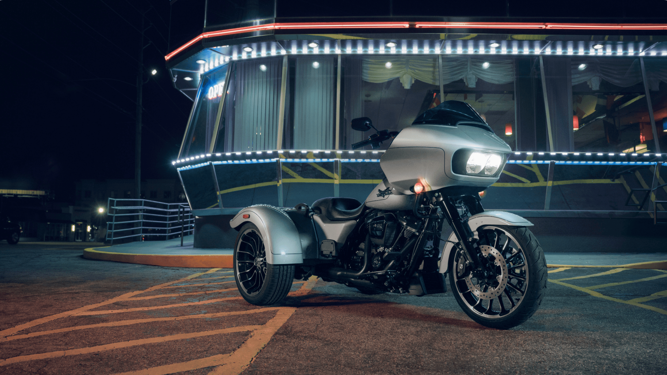 Silver 2025 Harley-Davidson Road Glide 3 trike parked at night near a diner with bright neon lights.