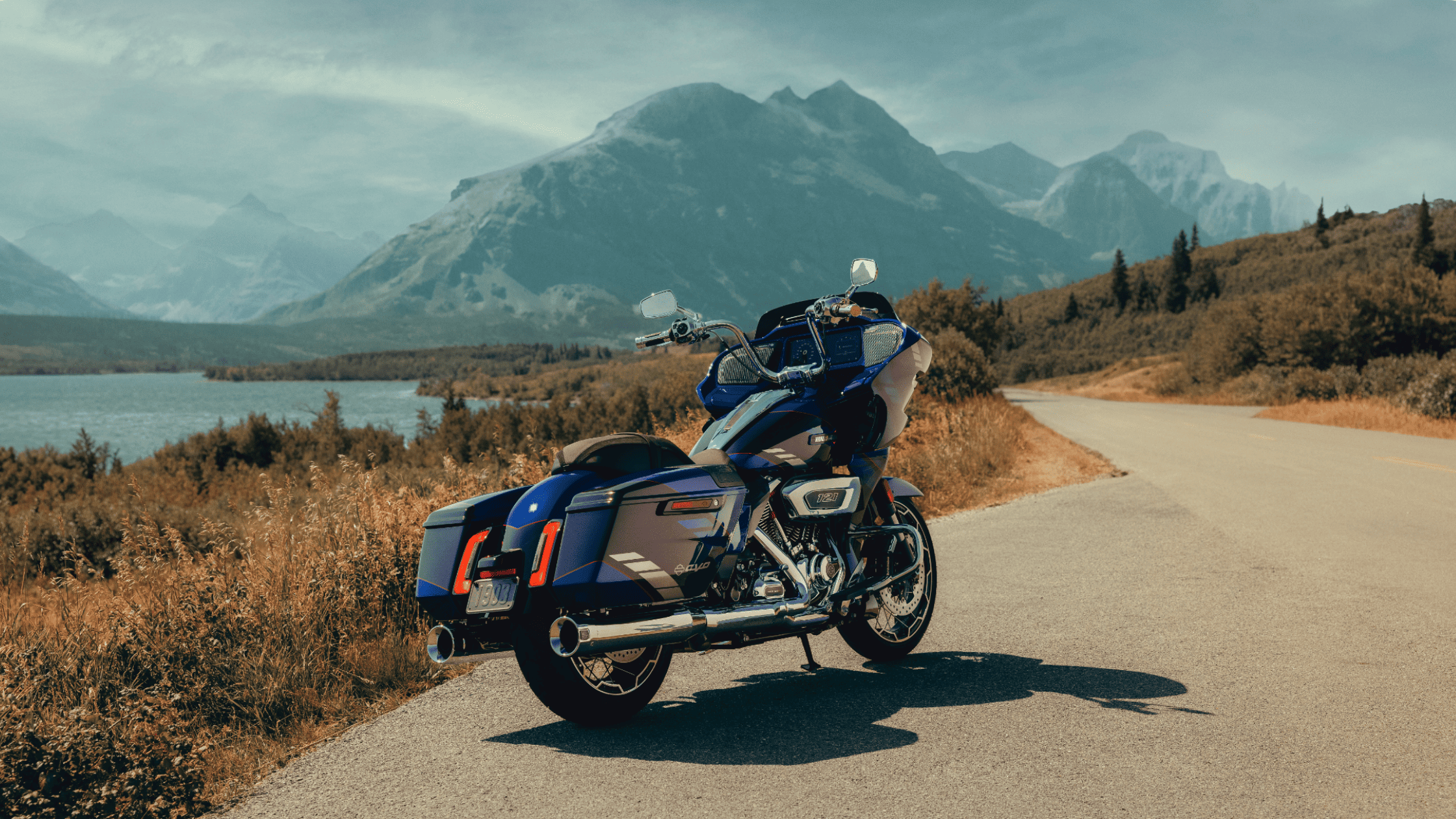 Blue 2025 Harley-Davidson CVO Road Glide touring motorcycle on a mountain road overlooking a lake.