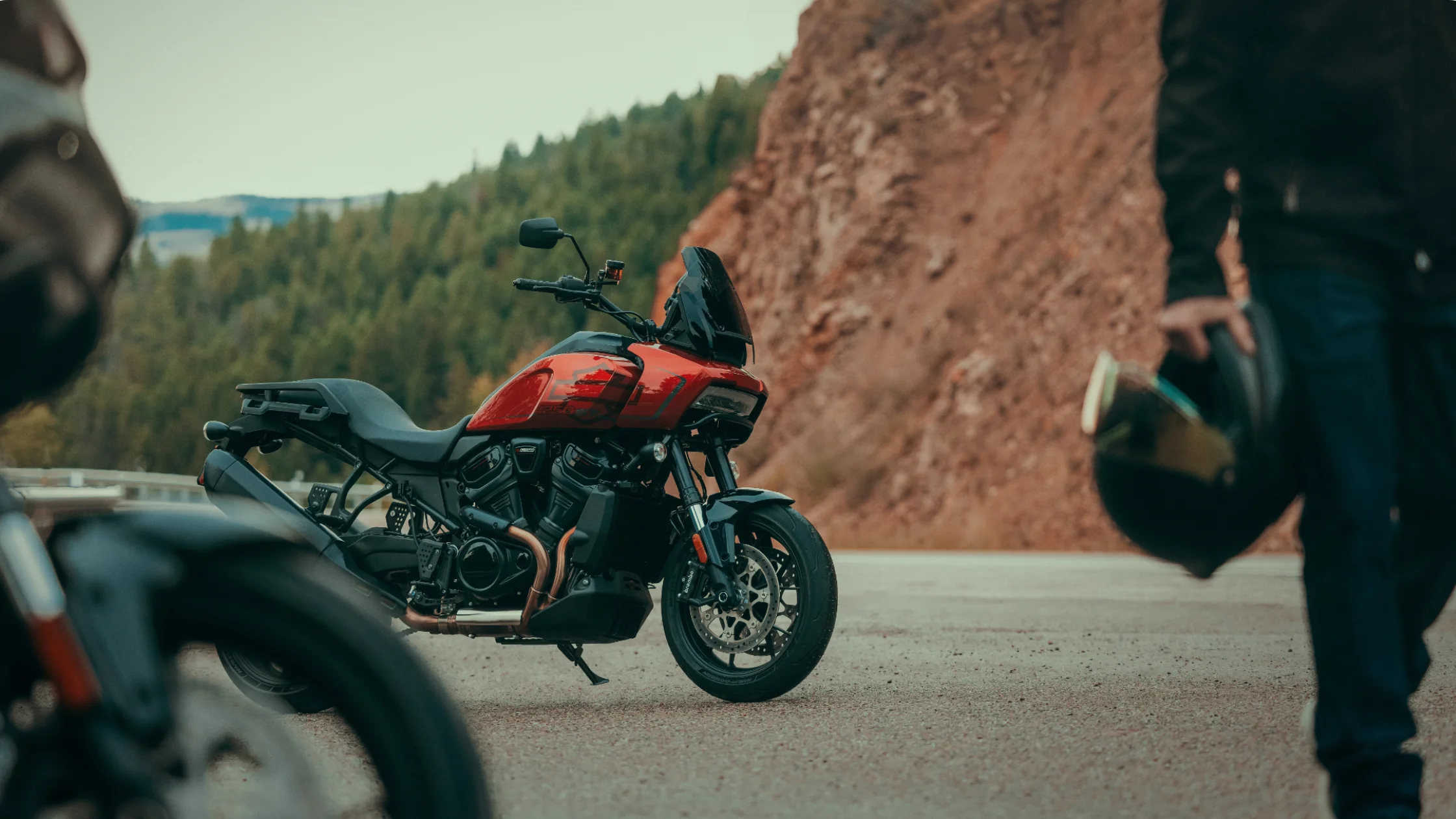 2025 Harley-Davidson® Pan America® 1250 ST in red parked by a mountain road with scenic rock backdrop.