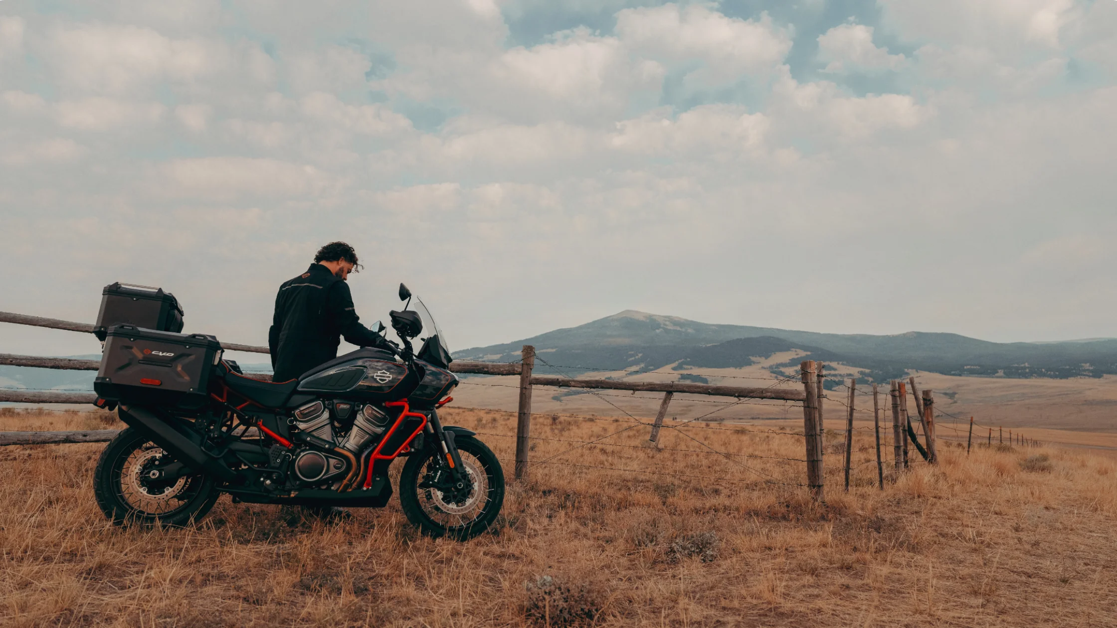 2025 Harley-Davidson® CVO™ Pan America® adventure bike with off-road gear parked on open grassland.