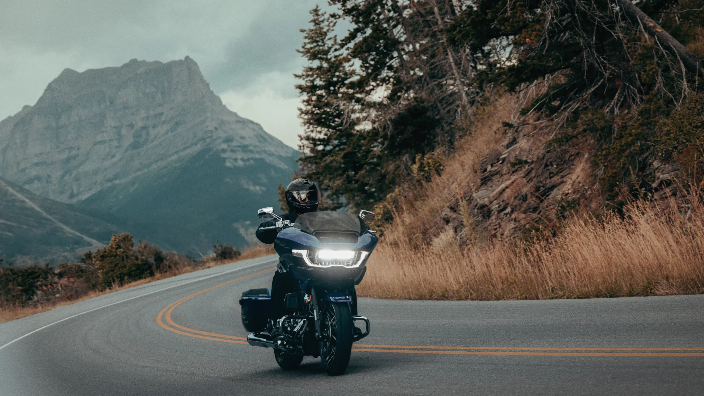 Rider on a blue 2025 Harley-Davidson CVO Road Glide cruising through mountain roads under cloudy skies.
