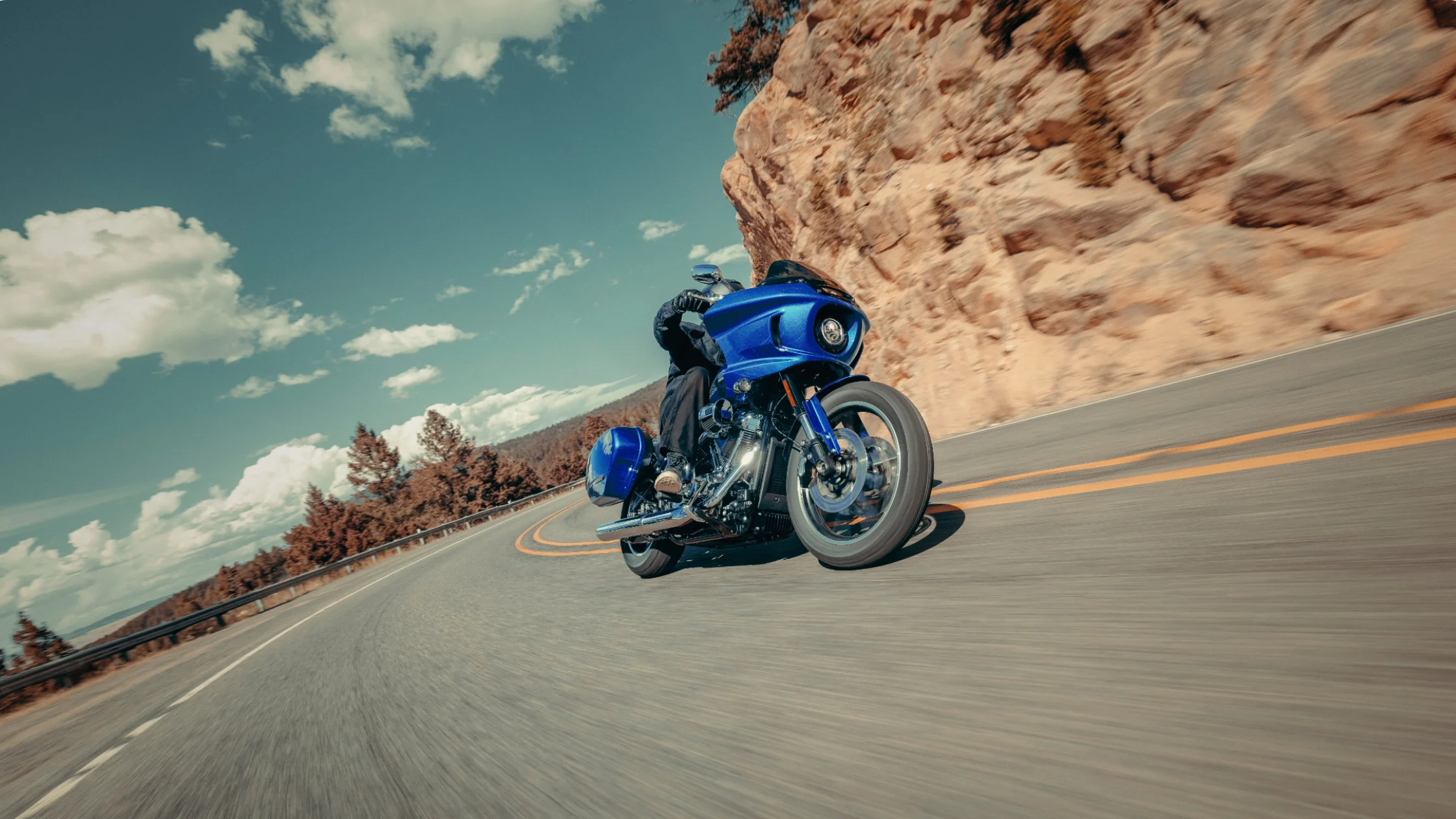 Rider on a blue 2025 Harley-Davidson Low Rider ST leaning into a mountain curve under a clear blue sky.