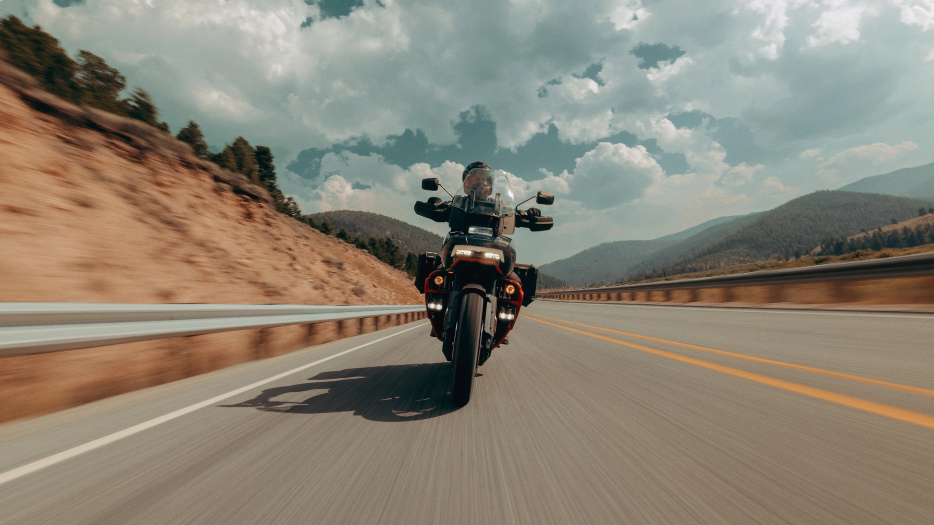 A rider jumps the 2025 Harley-Davidson® CVO™ Pan America® off-road through rocky terrain, showcasing its rugged tires, suspension travel, and dirt-ready performance.