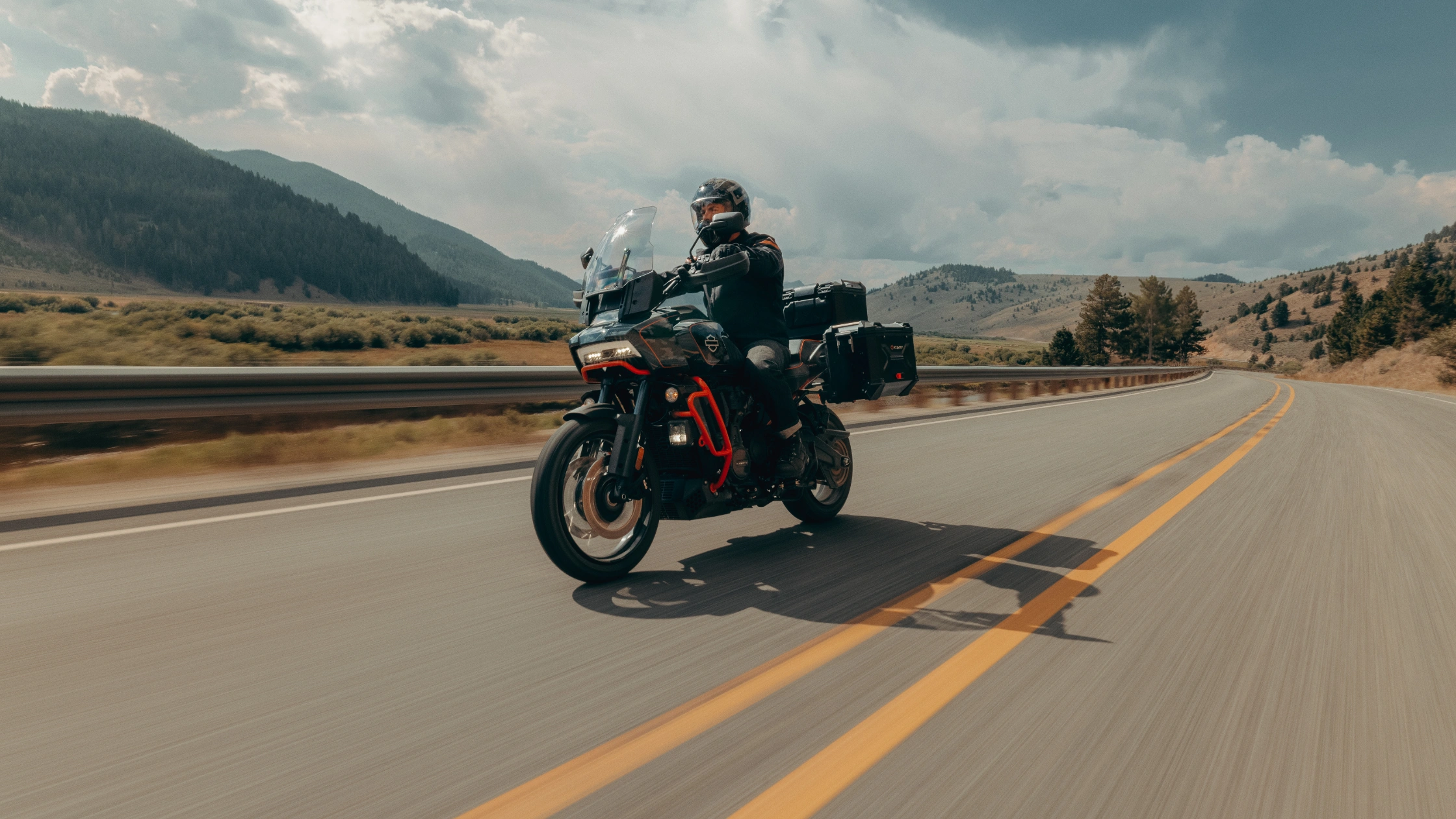 Rider cruising a 2025 CVO Pan America on open highway with mountains and clear skies in the background.