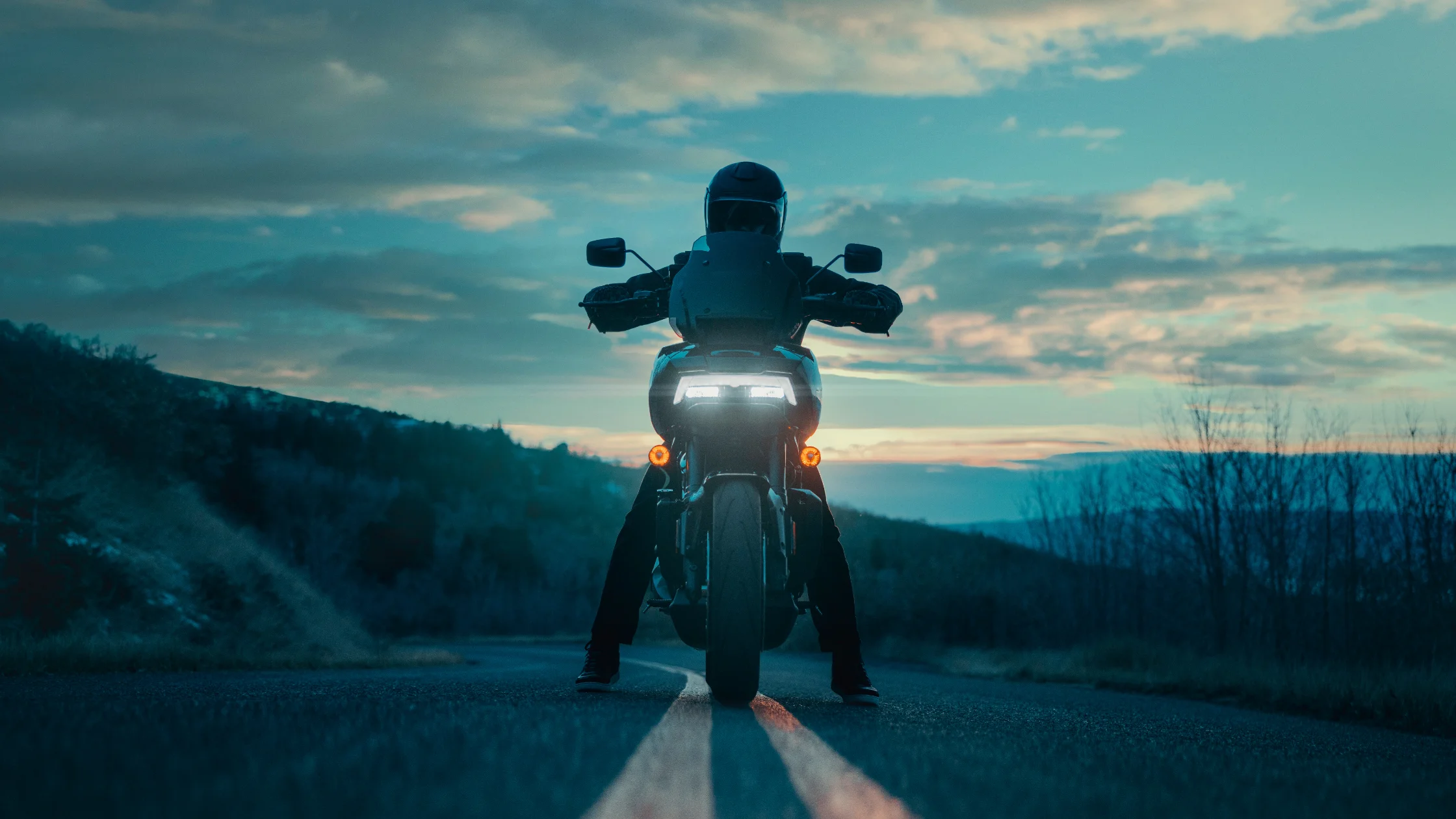 2025 Pan America® 1250 ST rider paused on mountain road at dusk with adventure-ready LED lighting.
