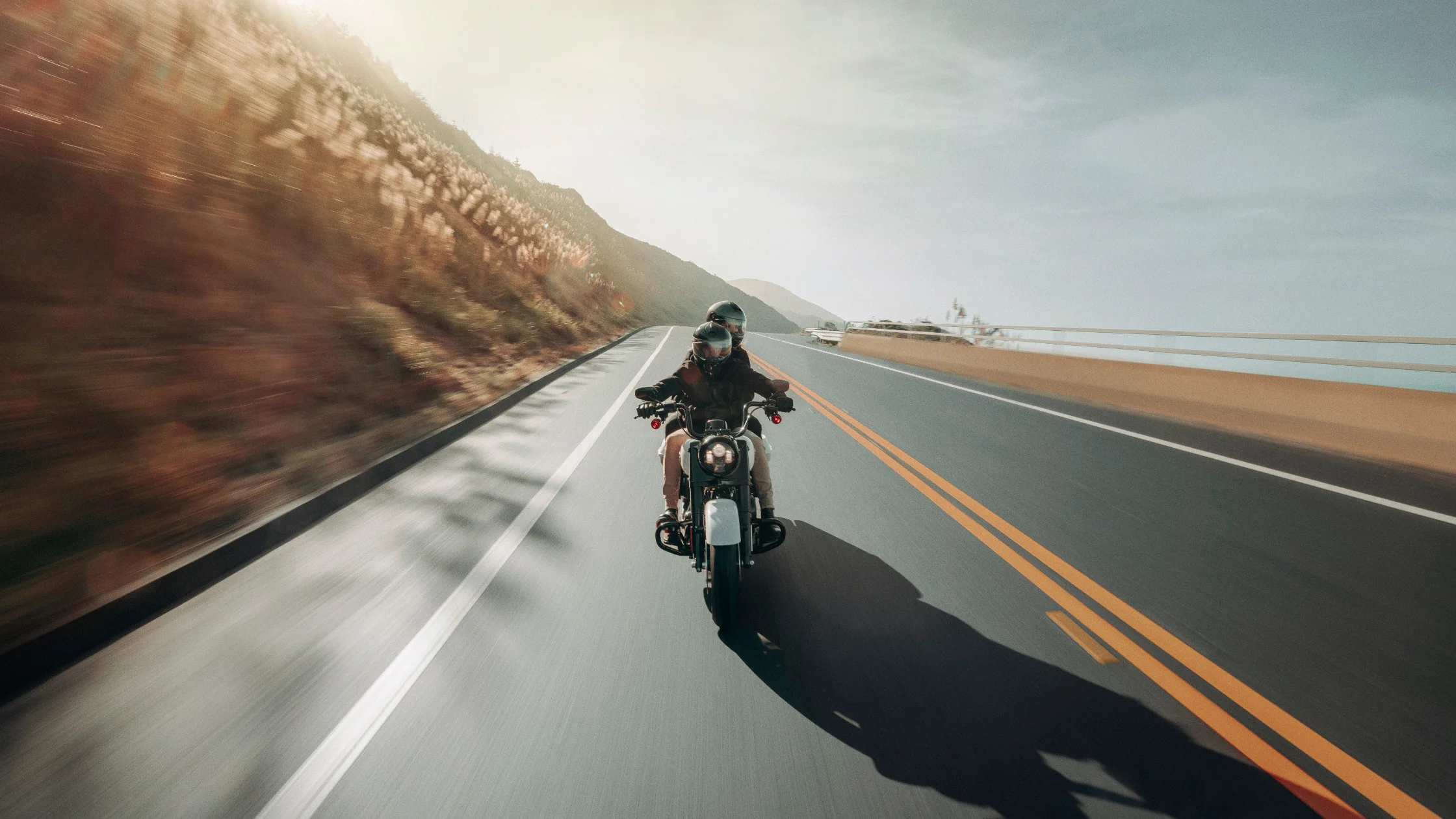 2025 H-D® Road King® Special carrying two riders along a bright coastal highway with hillside views