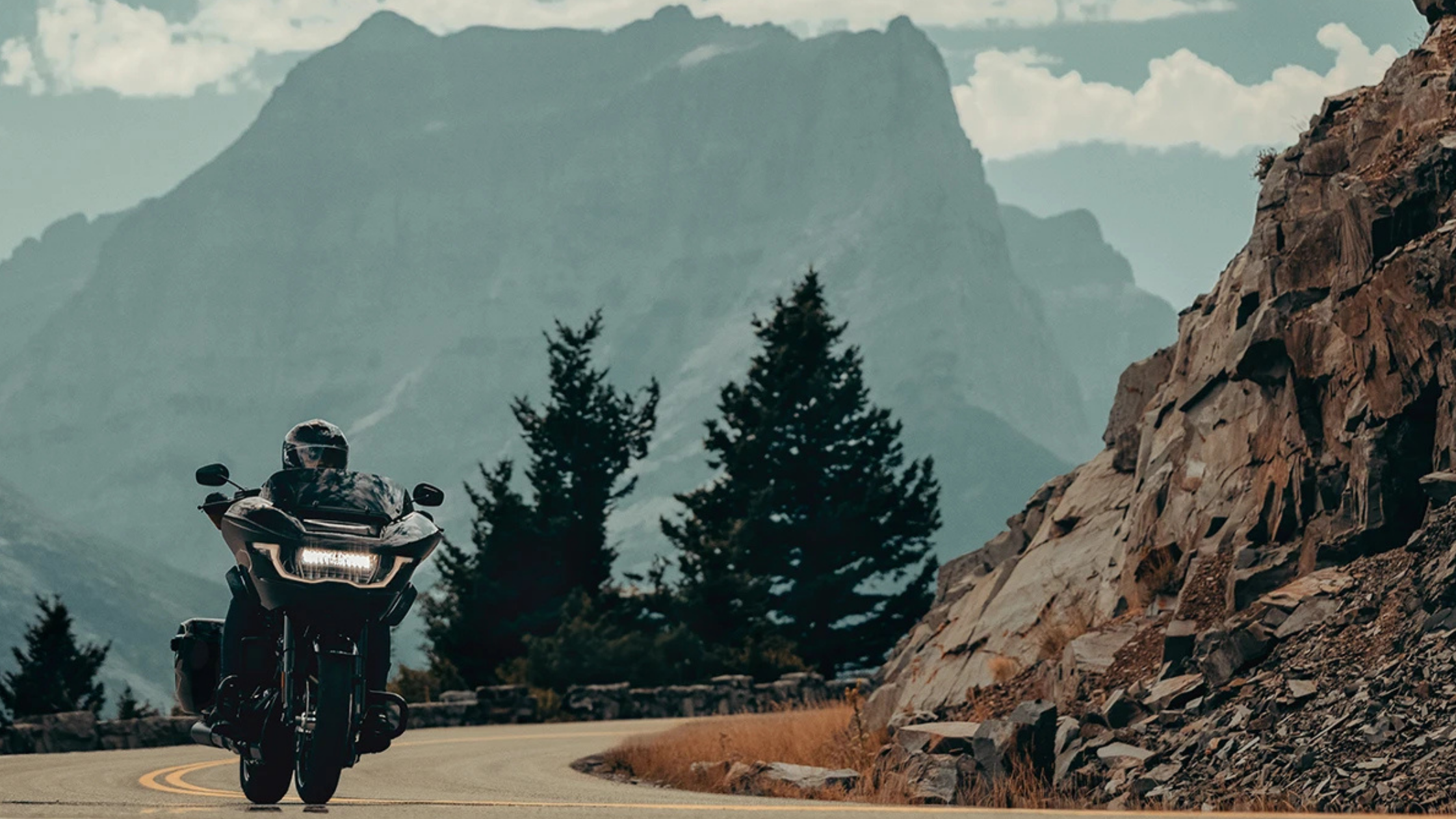 Front view of a 2025 Harley-Davidson® Road Glide® riding through mountain terrain with rocky cliffs in the background.