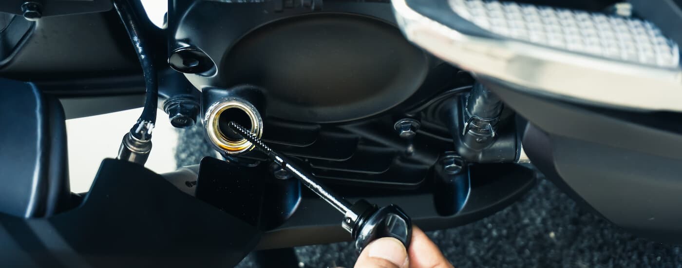 A close up of a person checking the oil stick on a motorcycle is shown at a motorcycle dealer.