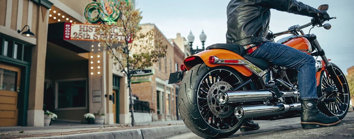 A man is shown riding an orange 2023 Harley-Davidson Breakout 117 after leaving a Harley-Davidson st…