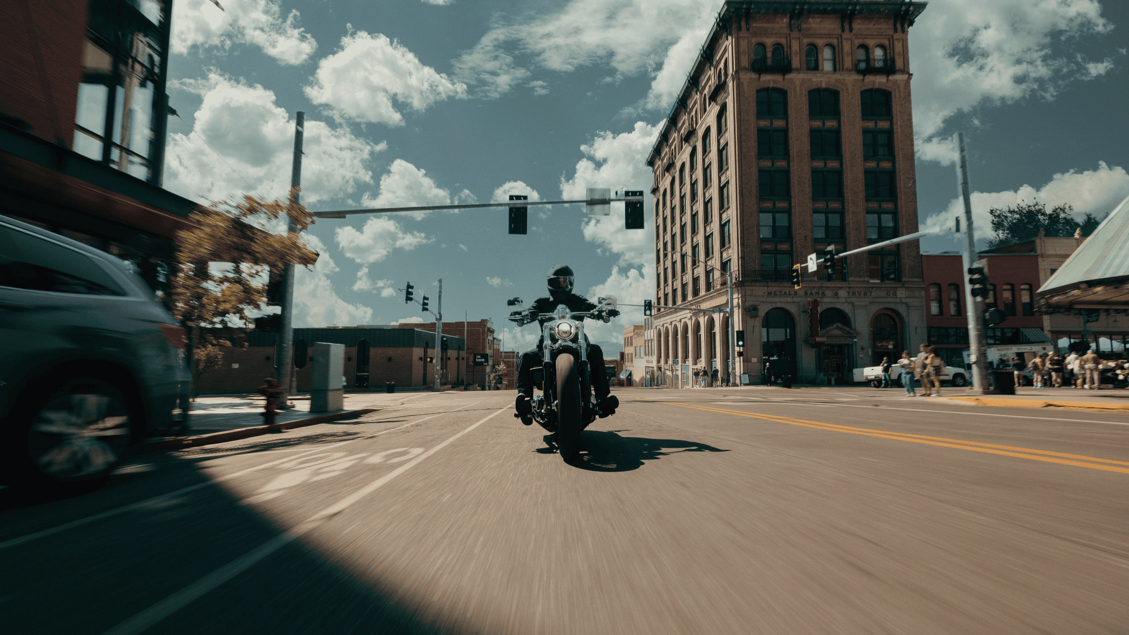 Front-facing view of a 2025 Harley-Davidson® Breakout® riding through a downtown street near Bentonville, AR, highlighting its wide front tire, stretched stance, and muscular cruiser design.