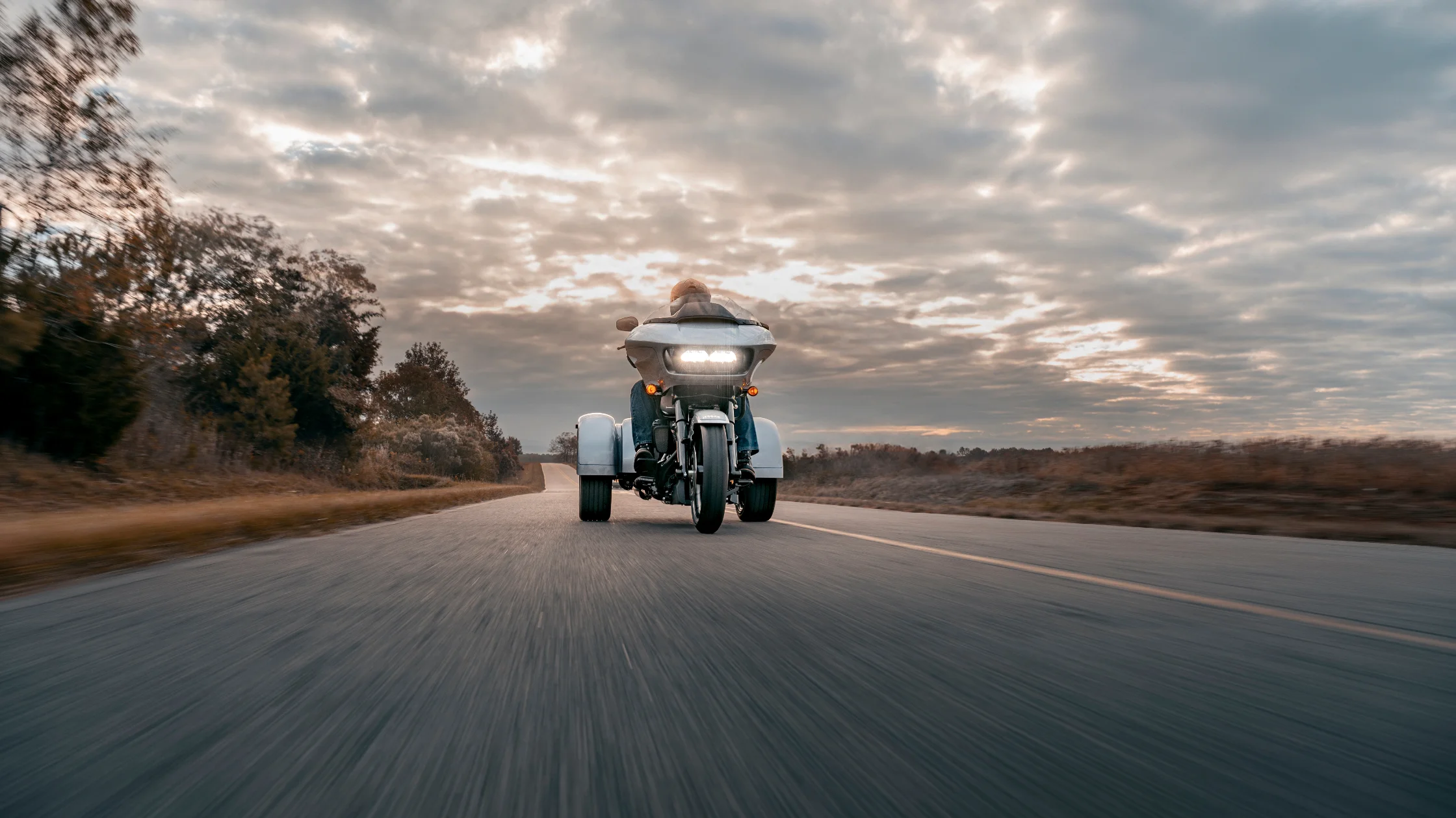 2025 Harley-Davidson® Road Glide® 3 trike riding highway at dusk with touring fairing