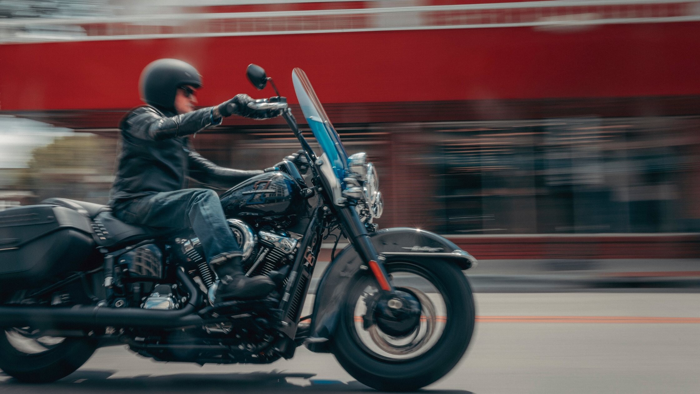 Rider on black 2026 Harley-Davidson® Heritage Classic cruising city street with windshield and bags