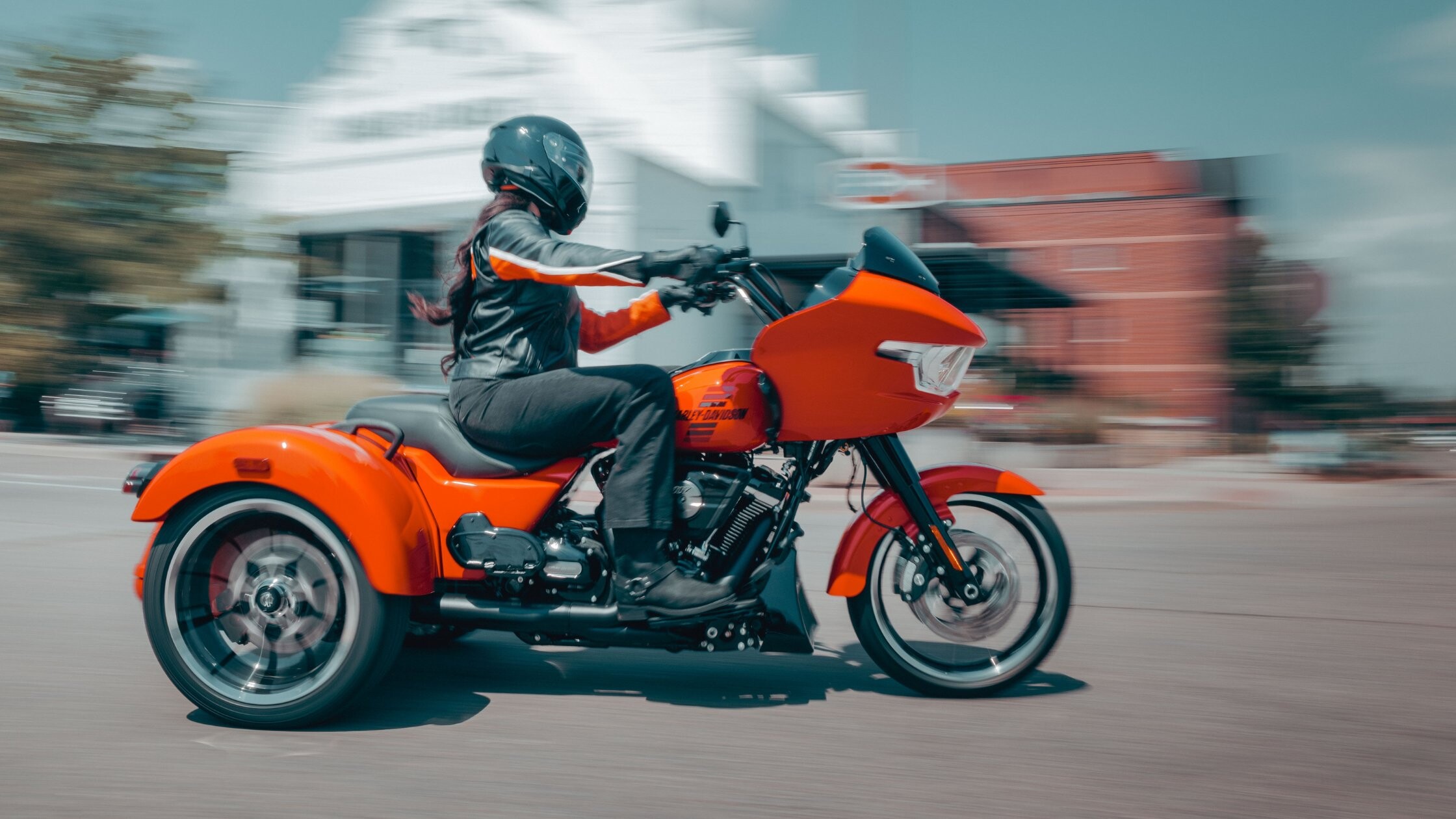 Orange 2026 Harley-Davidson® Road Glide® 3 rolling through downtown street with solo rider