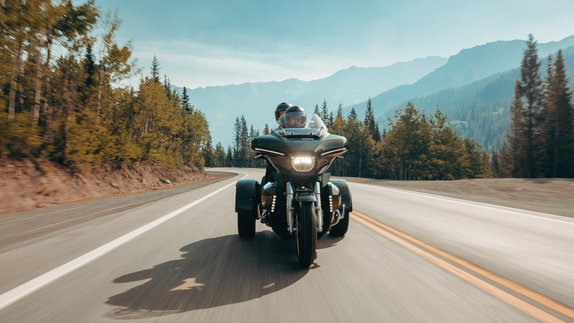 Front view of a 2026 Harley-Davidson® Street Glide® 3 Limited trike riding on a scenic mountain highway.