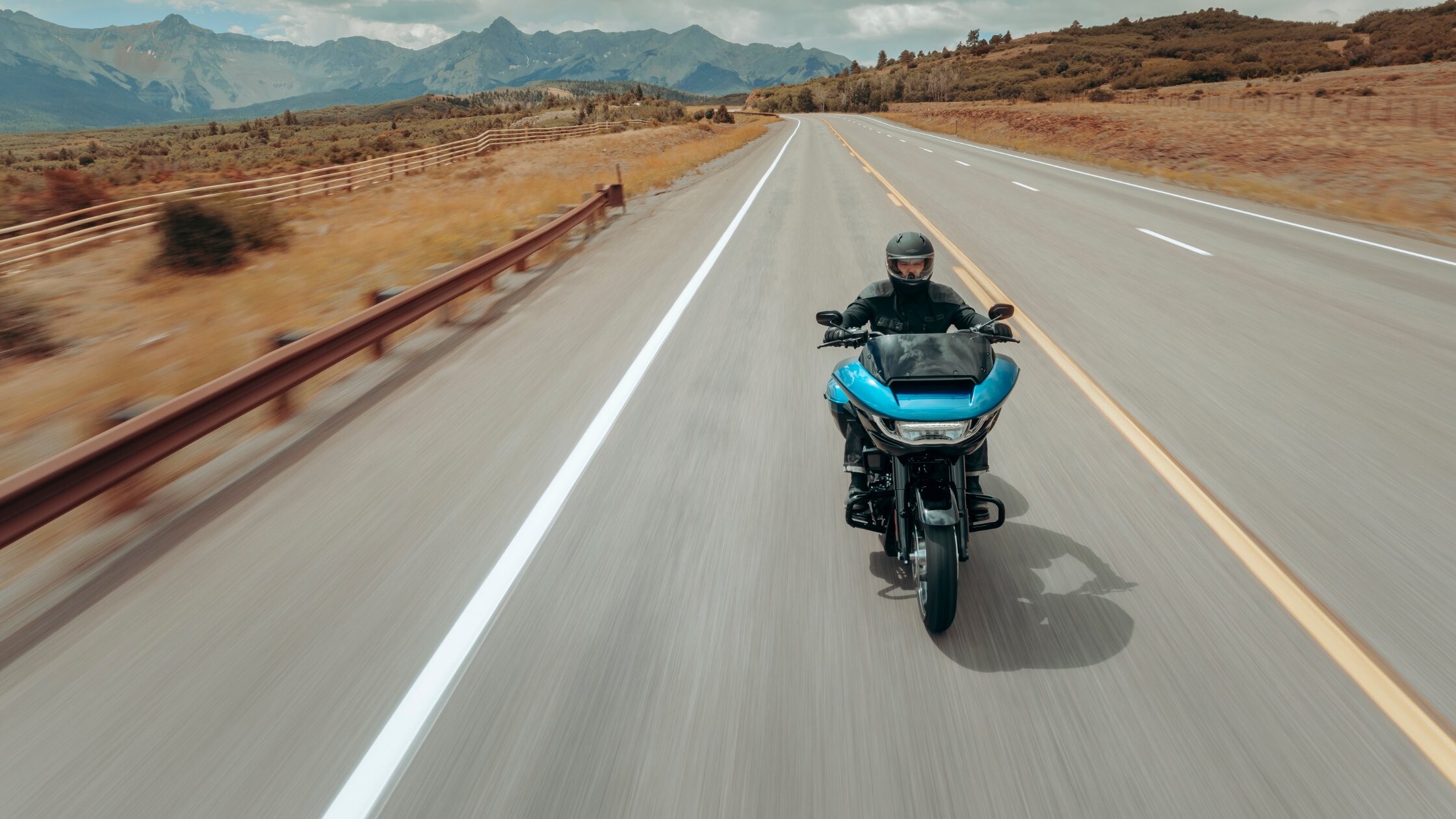 2026 Harley-Davidson® Road Glide® touring motorcycle rider cruising on an open highway with mountain views.