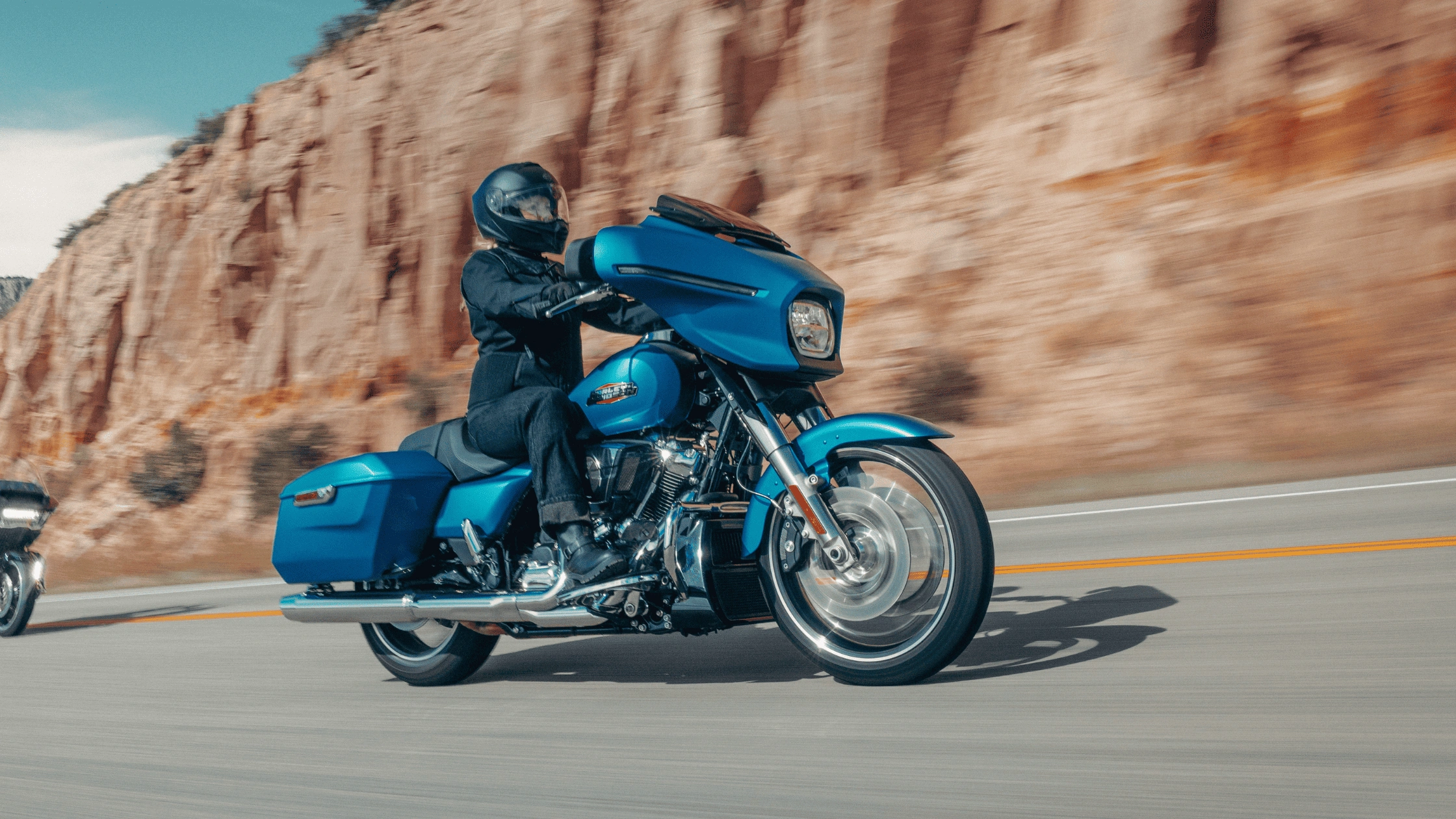 Rider on a blue 2026 Harley-Davidson Street Glide speeding past red rock cliffs in Baton Rouge, LA.