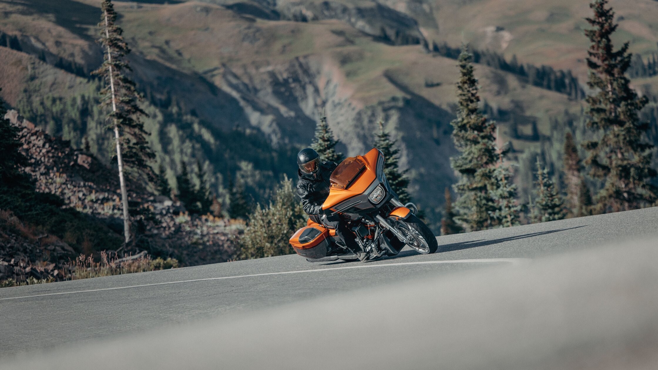Rider leans a 2026 H-D® CVO™ Street Glide® through a mountain curve with alpine views behind