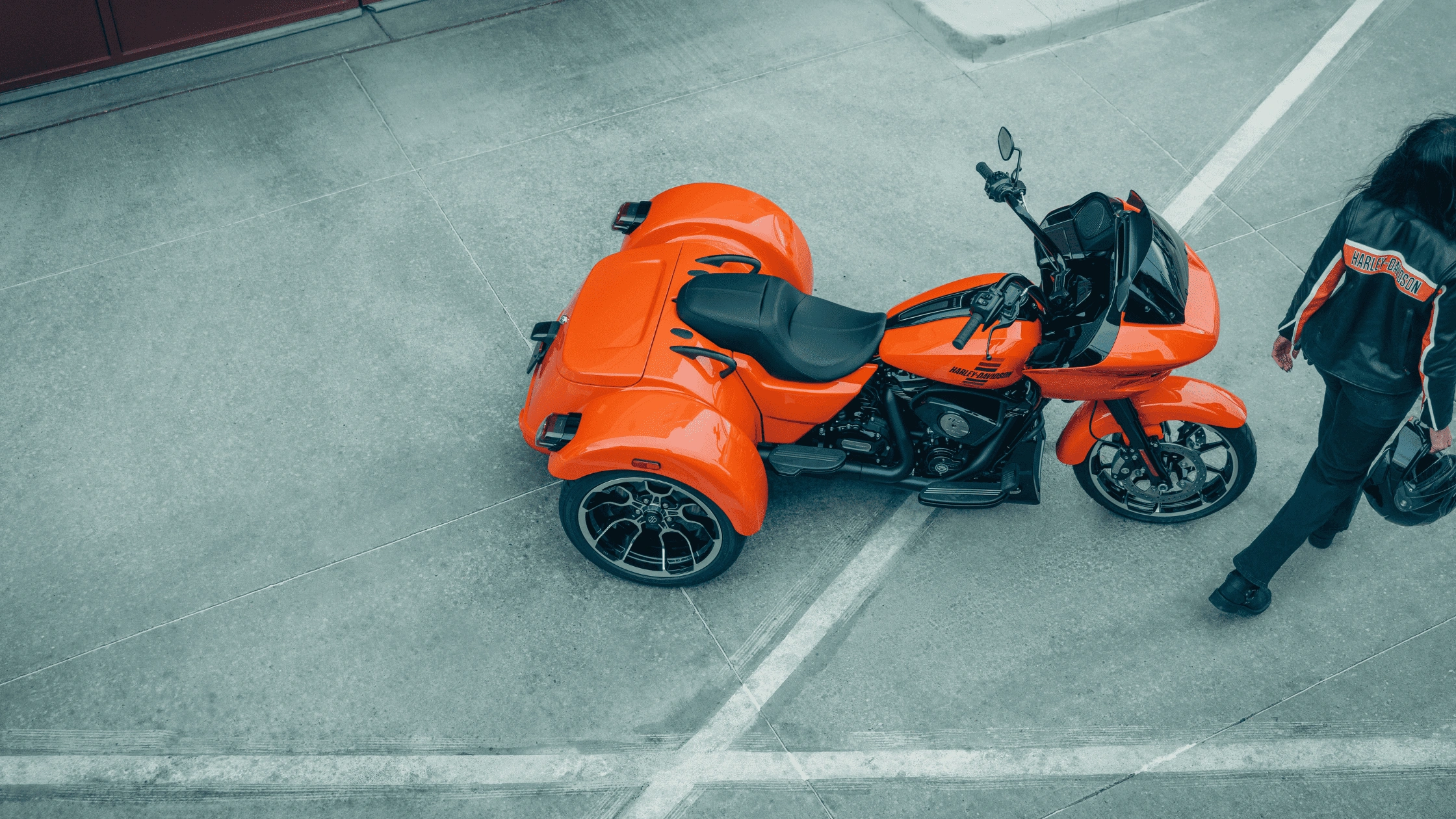 Aerial view of an orange 2026 Harley-Davidson Road Glide 3 trike with a female rider nearby in Bentonville, AR.