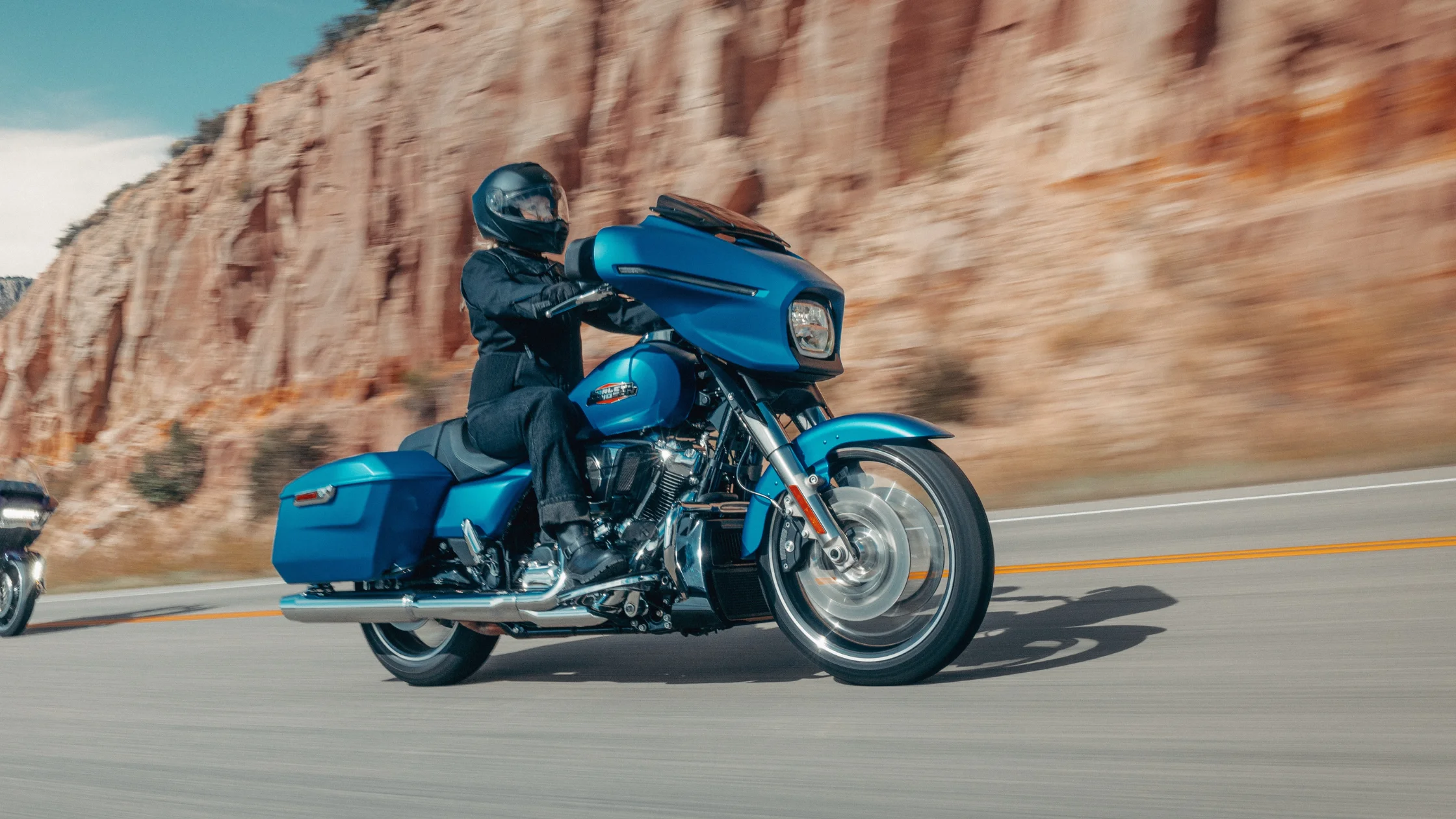 Rider on a blue 2026 H-D® Street Glide® cruising beside canyon cliffs on an open road