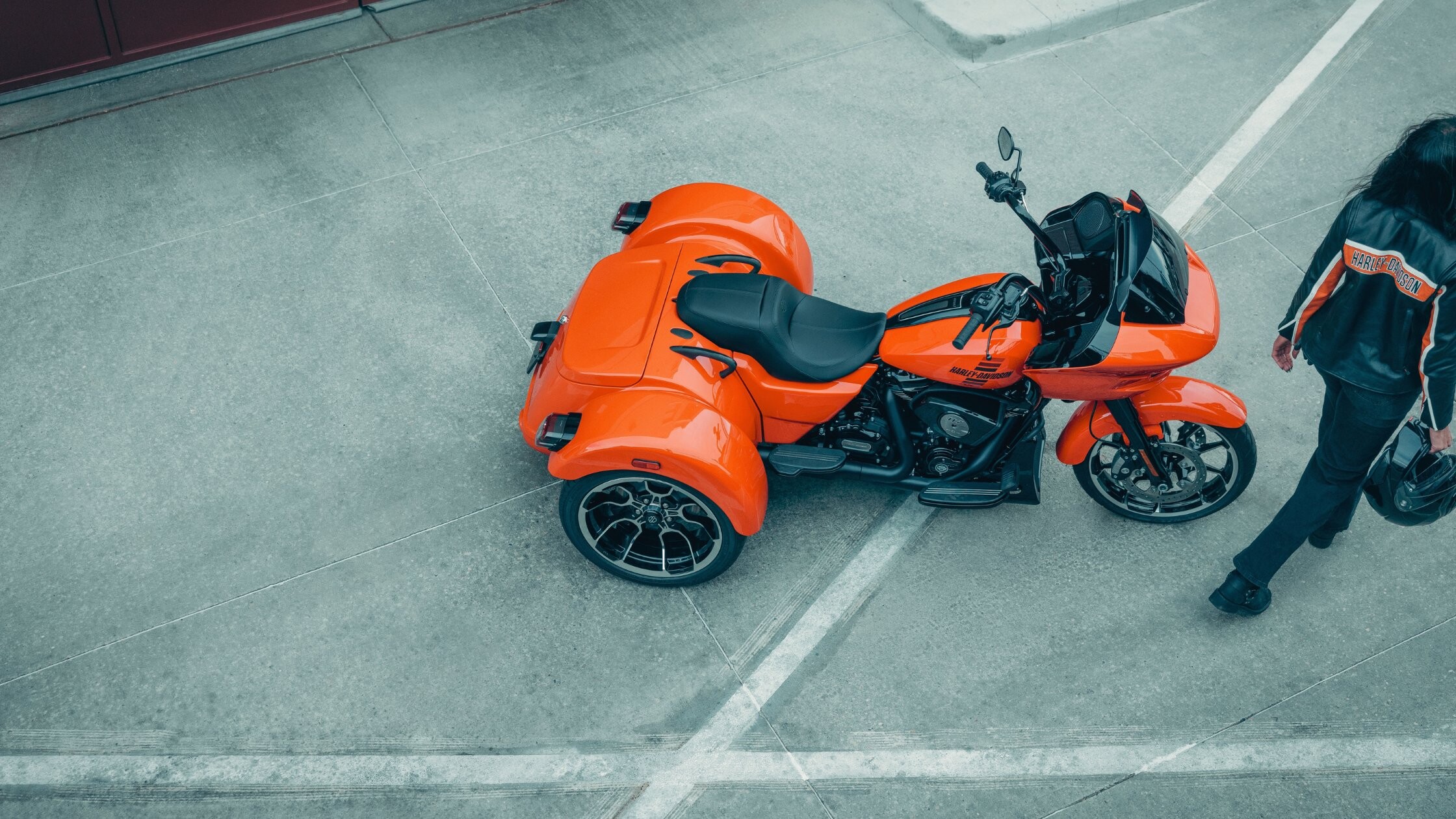 Orange 2026 H-D® Road Glide® 3 shown from above with rider walking beside the trike