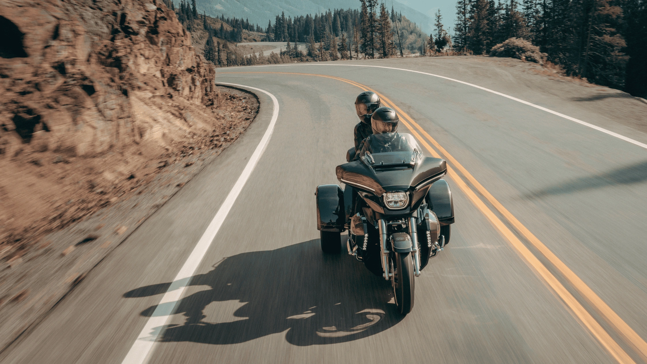 Two riders on a 2026 Harley-Davidson Street Glide 3 Limited trike in dark green navigating a winding mountain highway near Bentonville AR