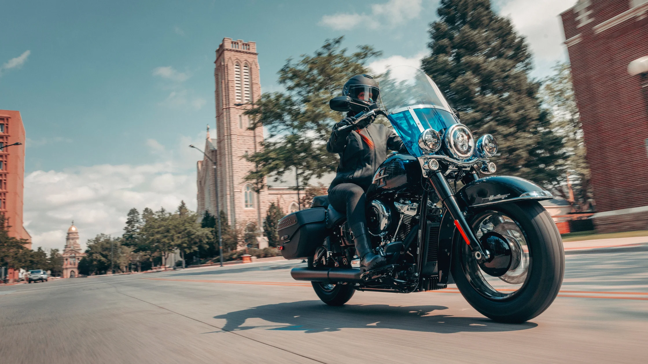 2026 H-D® Heritage Classic shown in motion near a church and downtown buildings