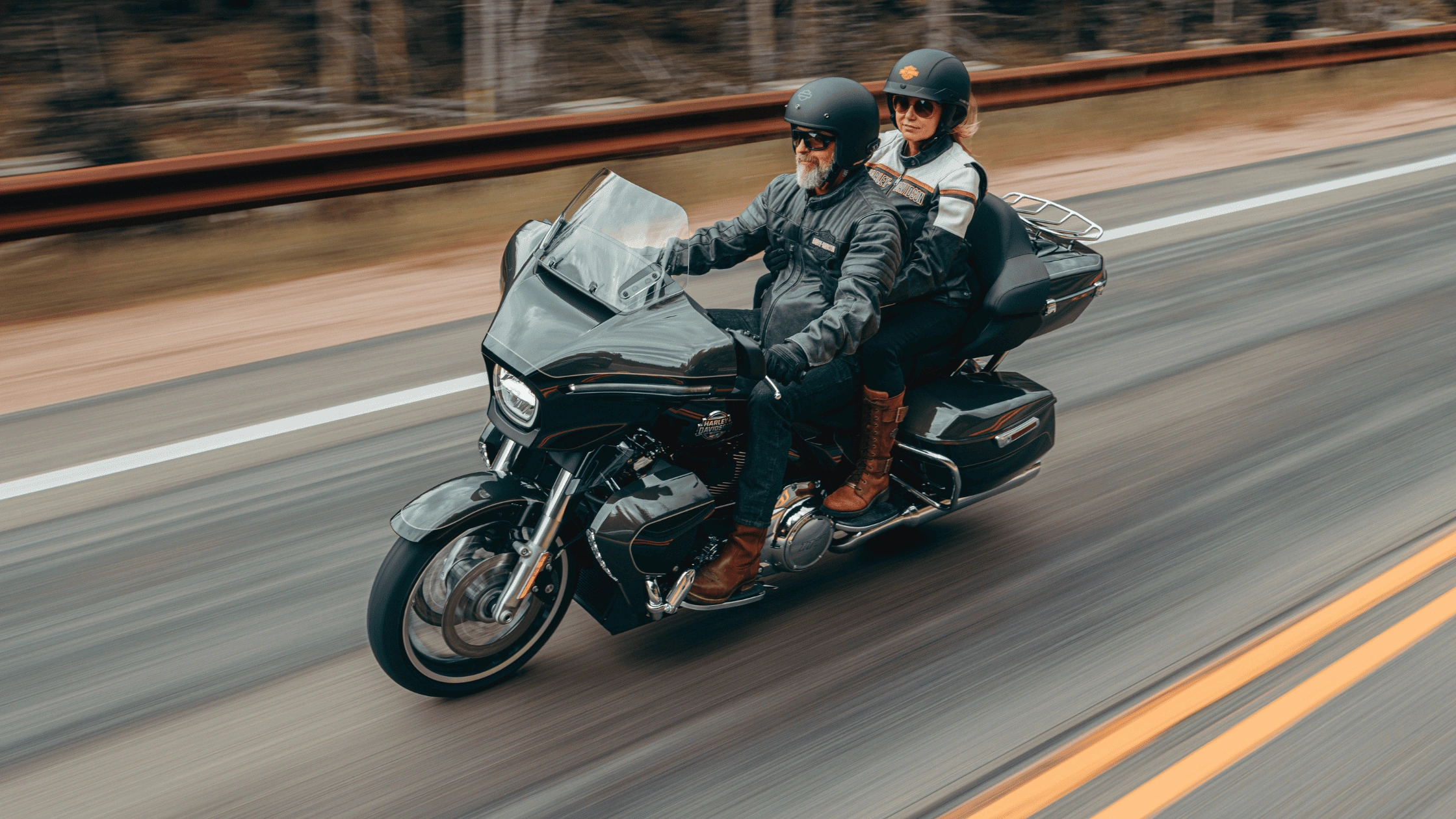 Couple riding a 2026 Harley-Davidson Street Glide Limited in black on a wooded highway showcasing two-up touring comfort, available in Baton Rouge LA