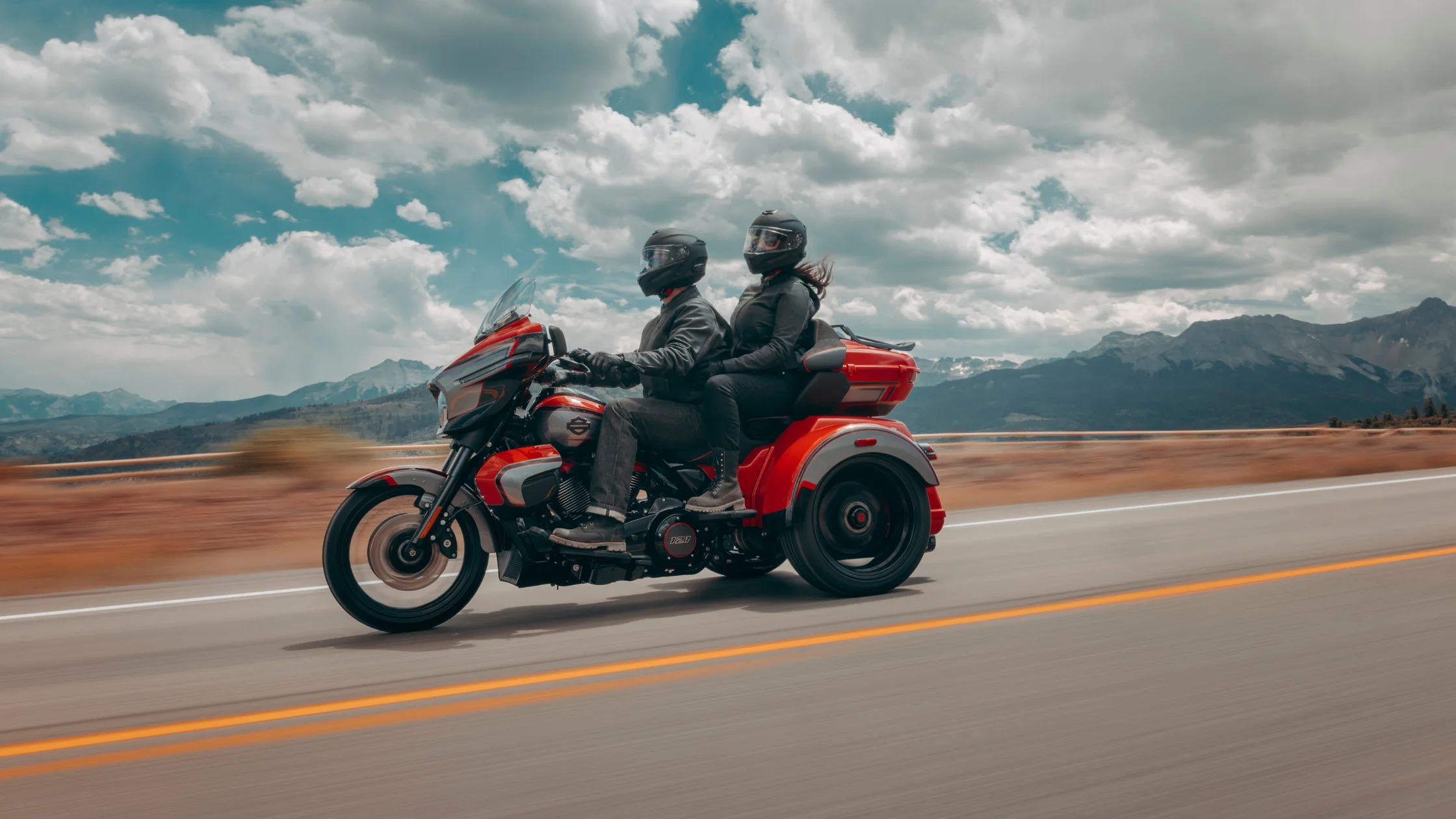 A couple rides a red 2026 H-D® CVO™ Street Glide® 3 Limited trike on a scenic high mountain highway.